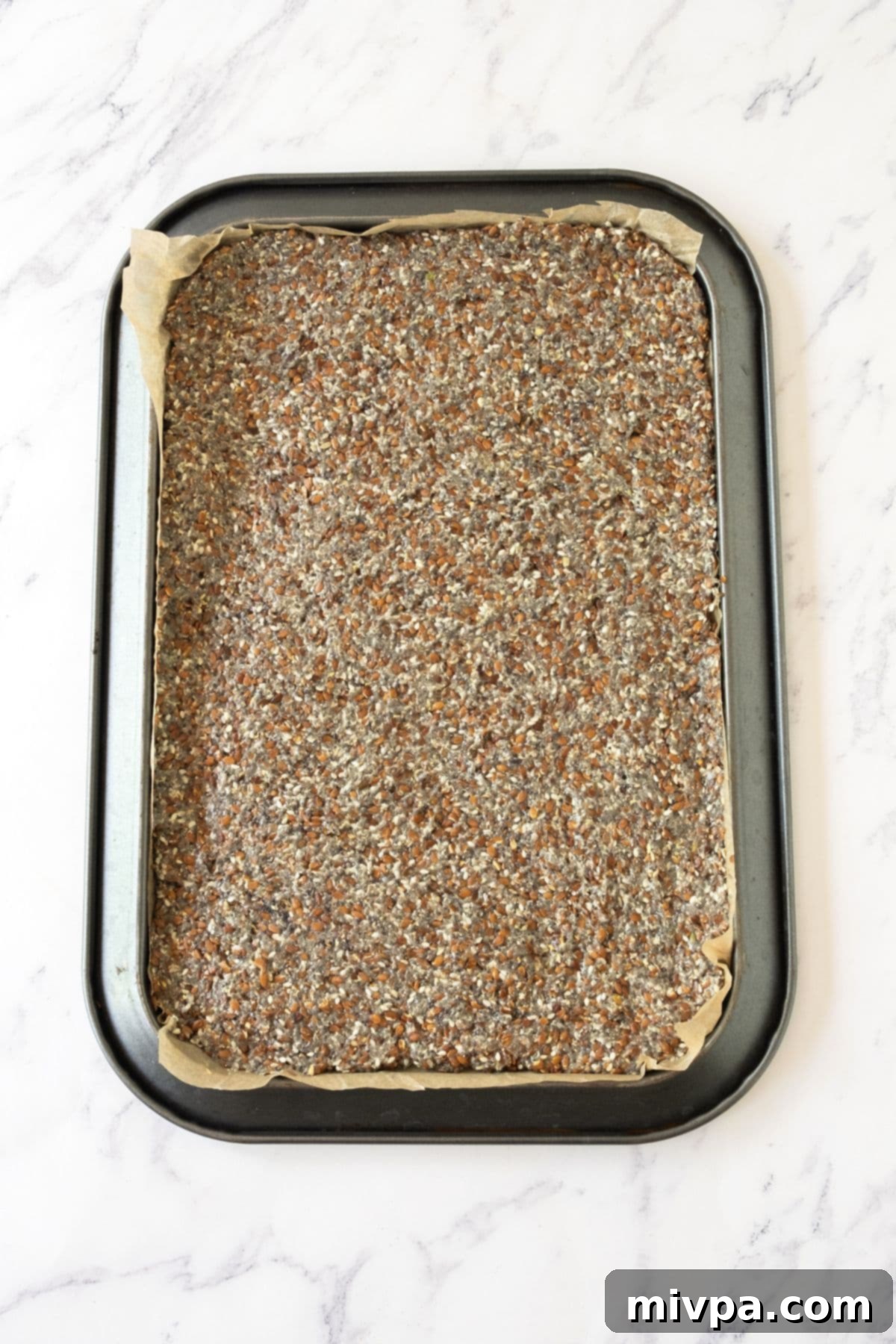 Effortless Gluten-Free Vegan Flaxseed Crackers 3 The flaxseed meal mixture uniformly pressed between two sheets of parchment paper on a baking sheet, ready for baking.