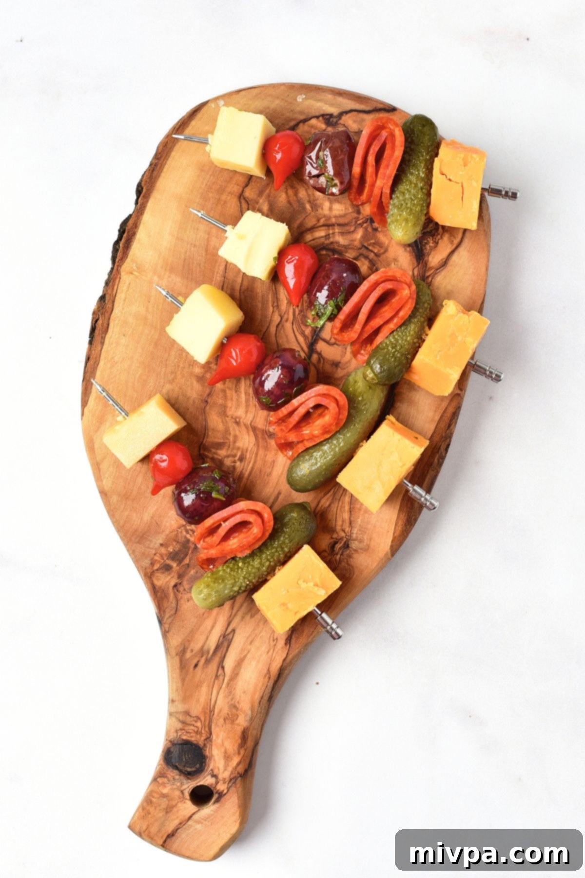 Partially assembled appetizer kabobs on a wooden board, showing the order of ingredients being threaded onto skewers.