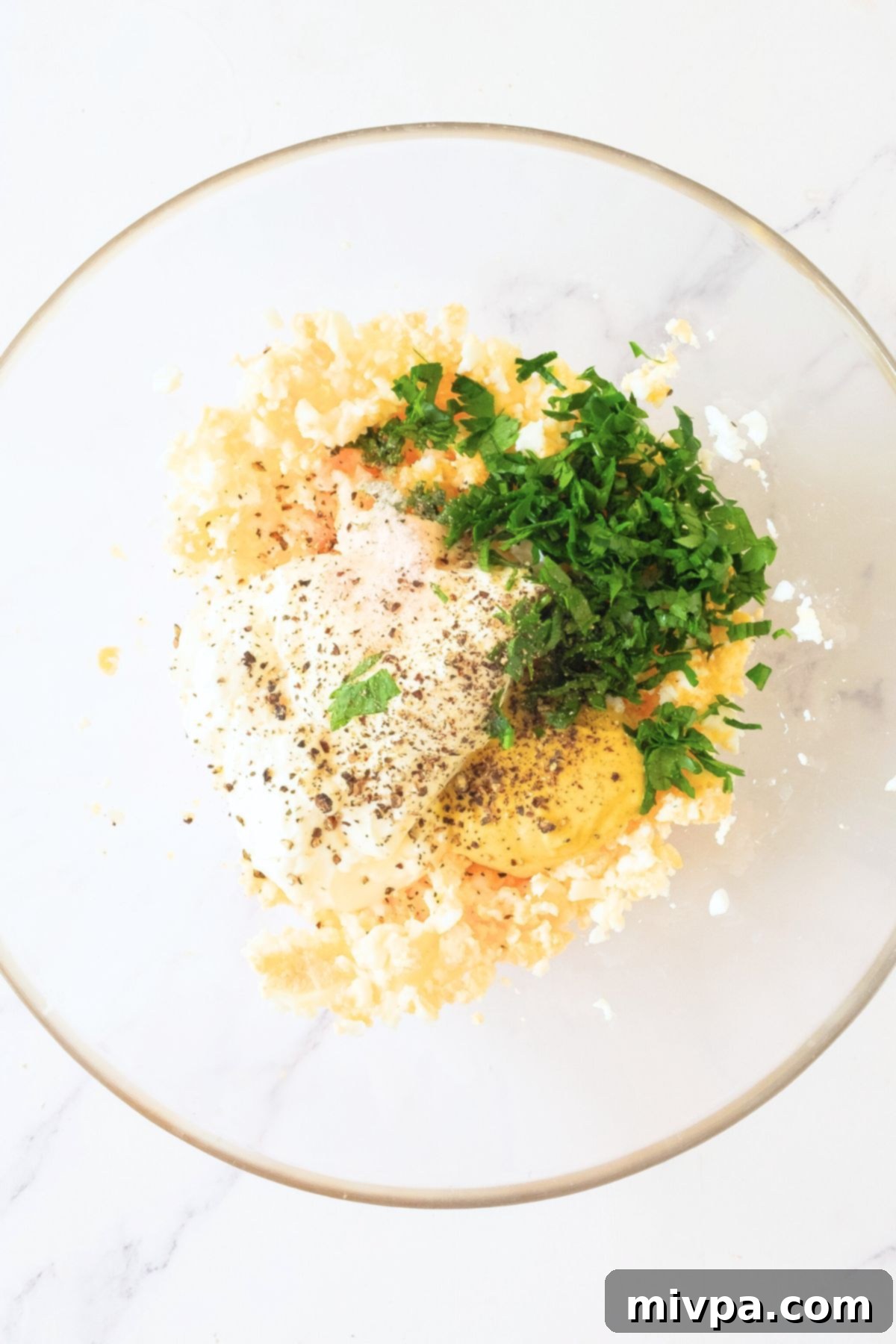 Chopped egg salad with chopped fresh parsley in a glass bowl.