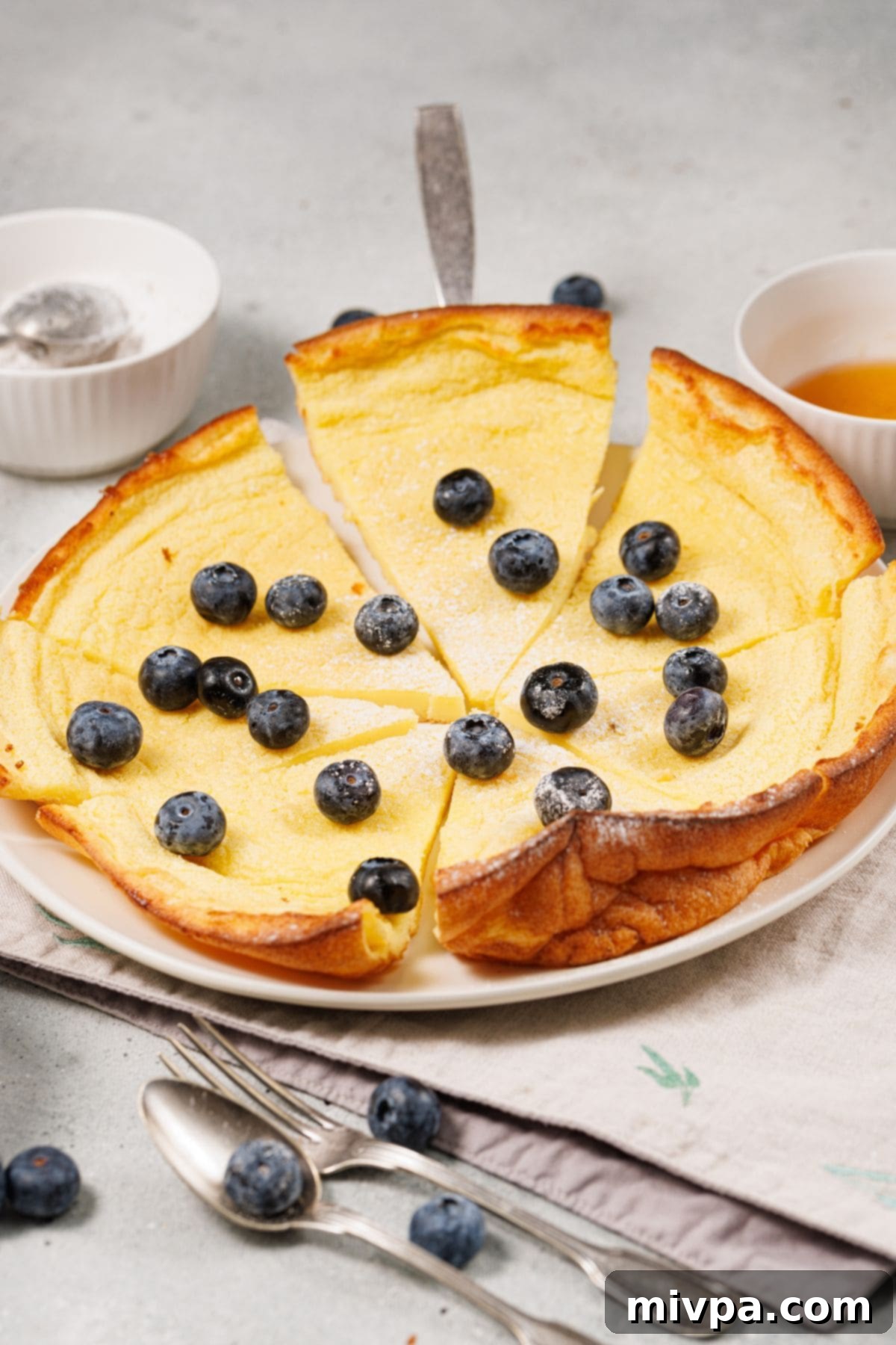 Easy Gluten-Free Dutch Pancakes (Dairy-Free) Sliced Dutch baby pancake topped with blueberries and powdered sugar.