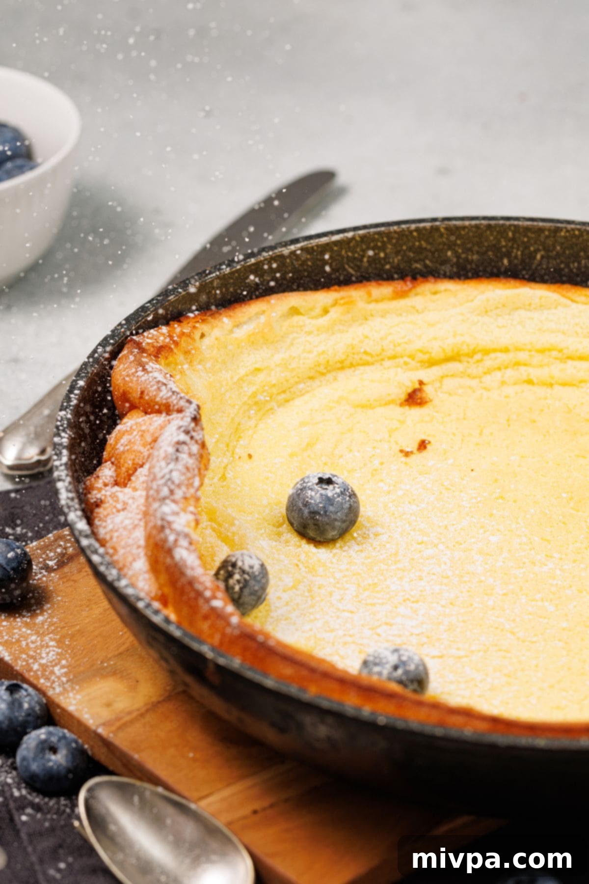 Easy Gluten-Free Dutch Baby Pancake (Dairy-Free) Gluten-free Dutch baby pancake in cast iron skillet sprinkled in powdered sugar.
