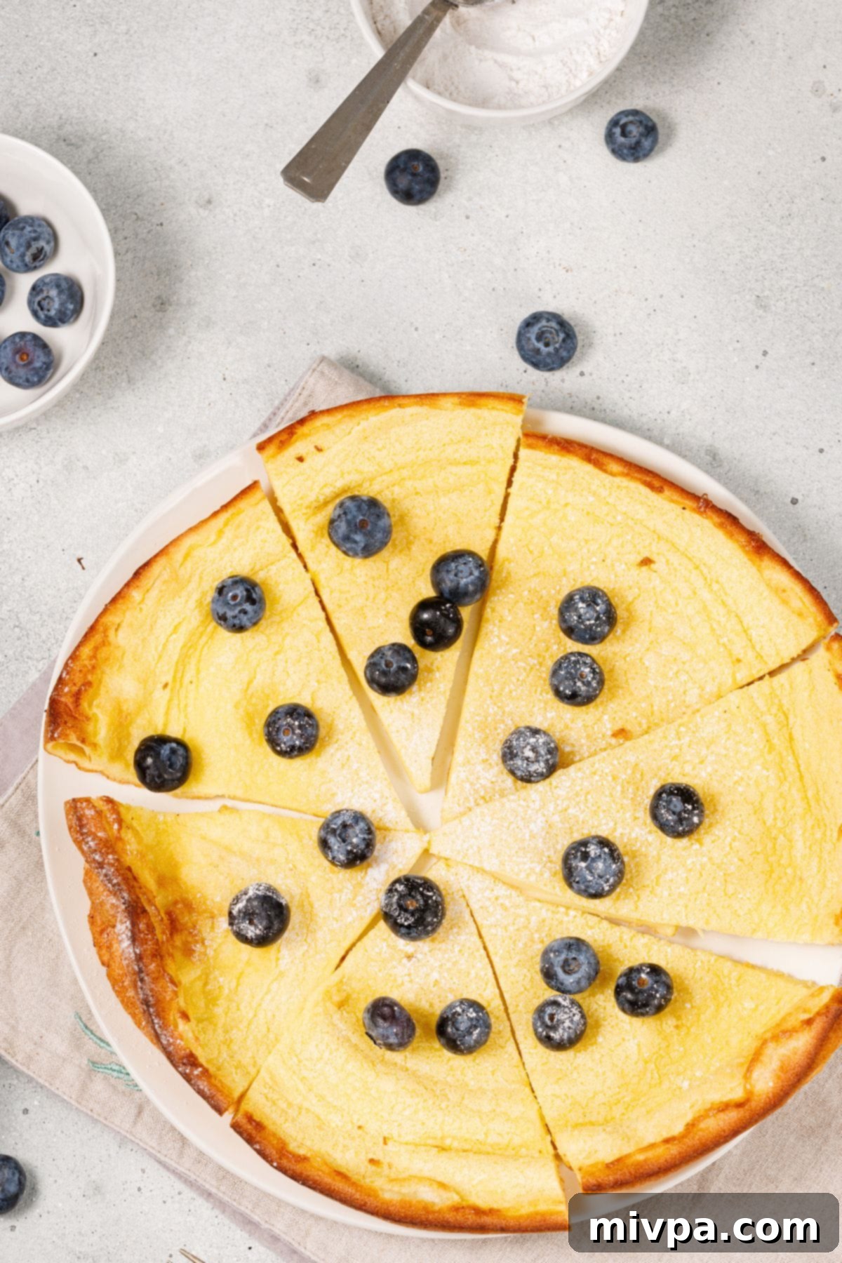 Easy Gluten-Free German Pancakes (Dairy-Free) Top down view of sliced gluten-free German pancakes topped with fresh blueberries.