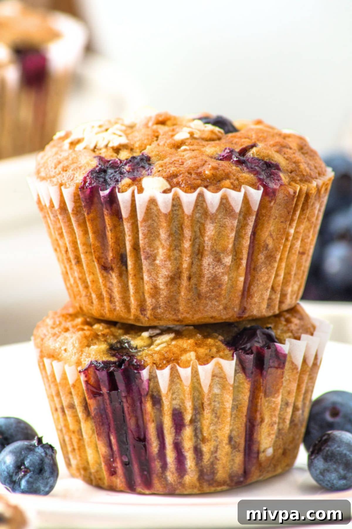 A stack of two banana blueberry oatmeal muffins on a plate, showcasing their moist texture and golden-brown tops.
