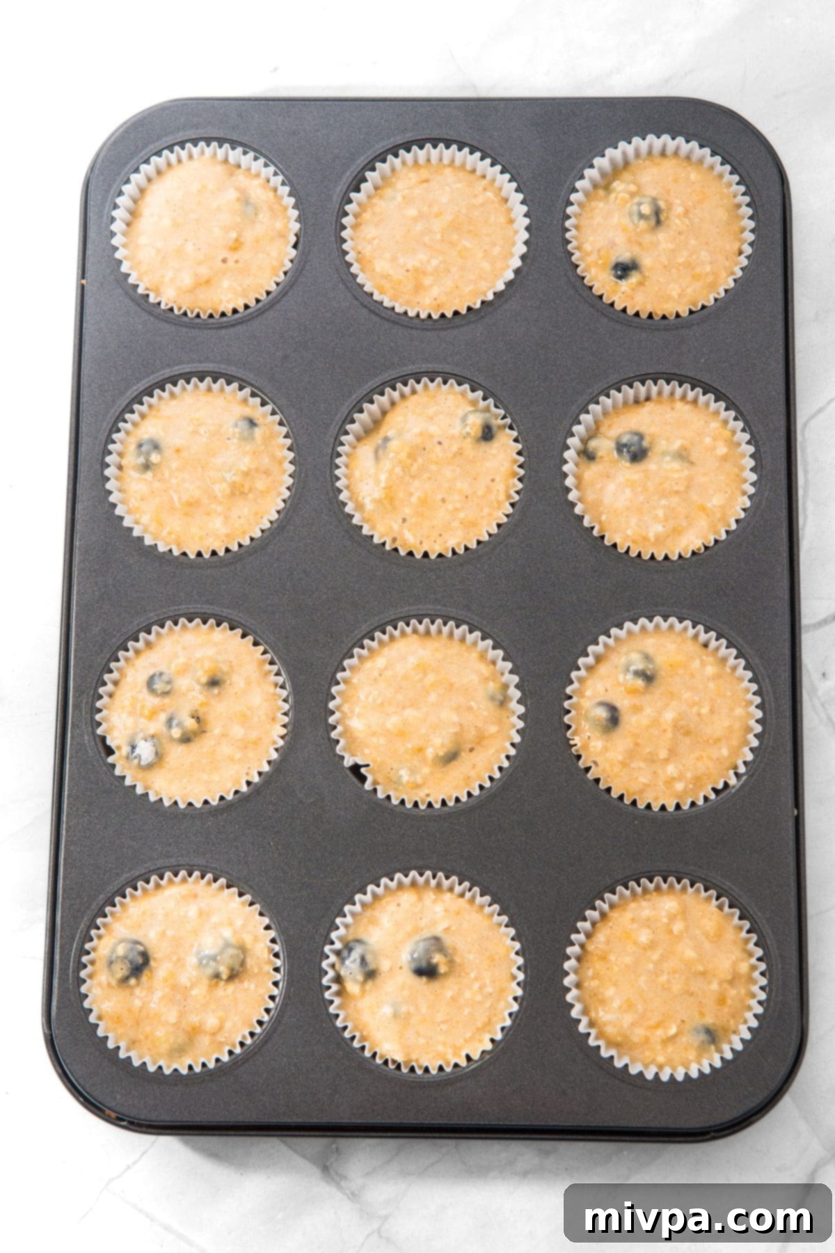 Muffin batter poured into paper-lined muffin pan cavities, ready for baking.