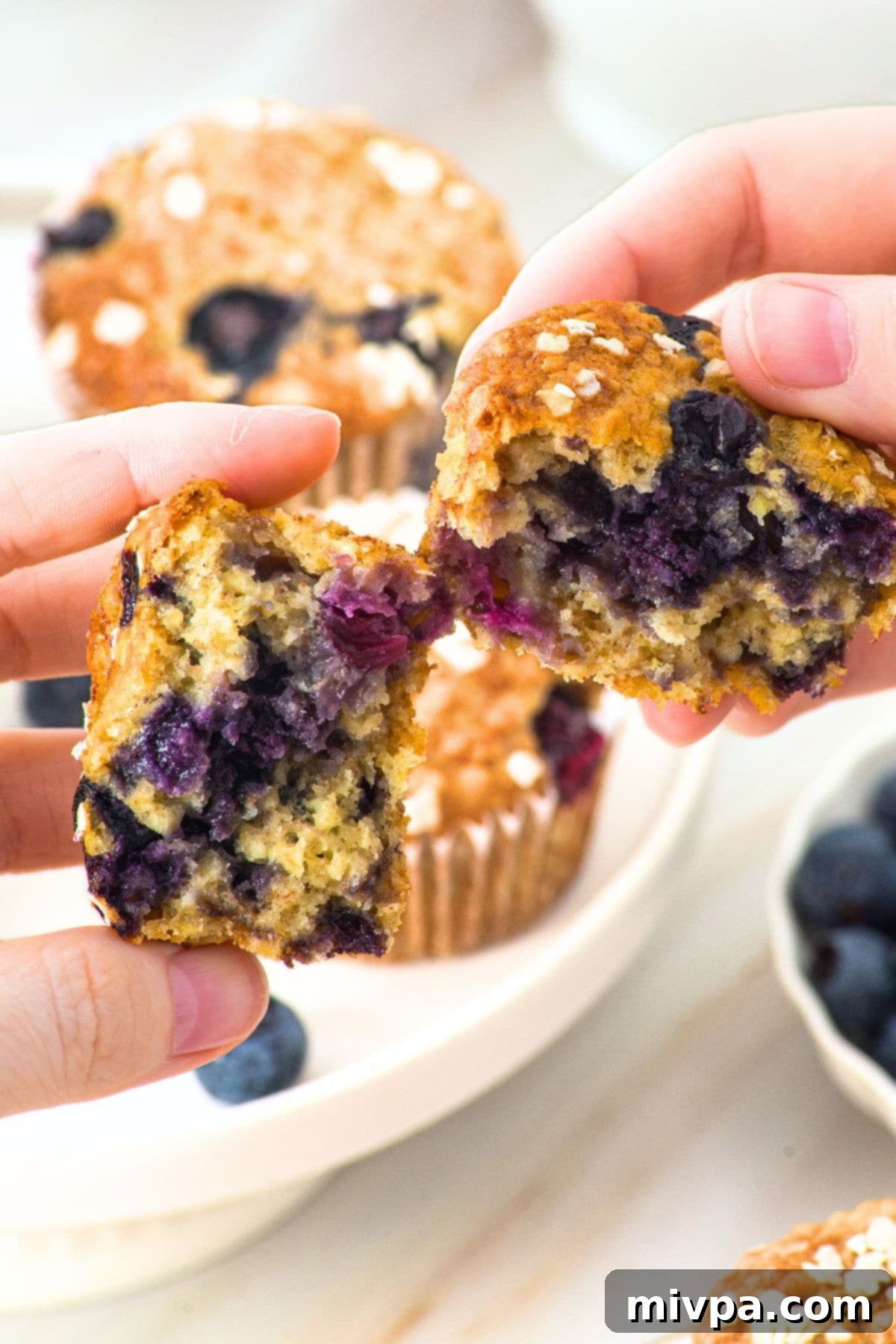 A close-up of a banana oatmeal blueberry muffin being pulled apart, revealing its soft, moist interior.