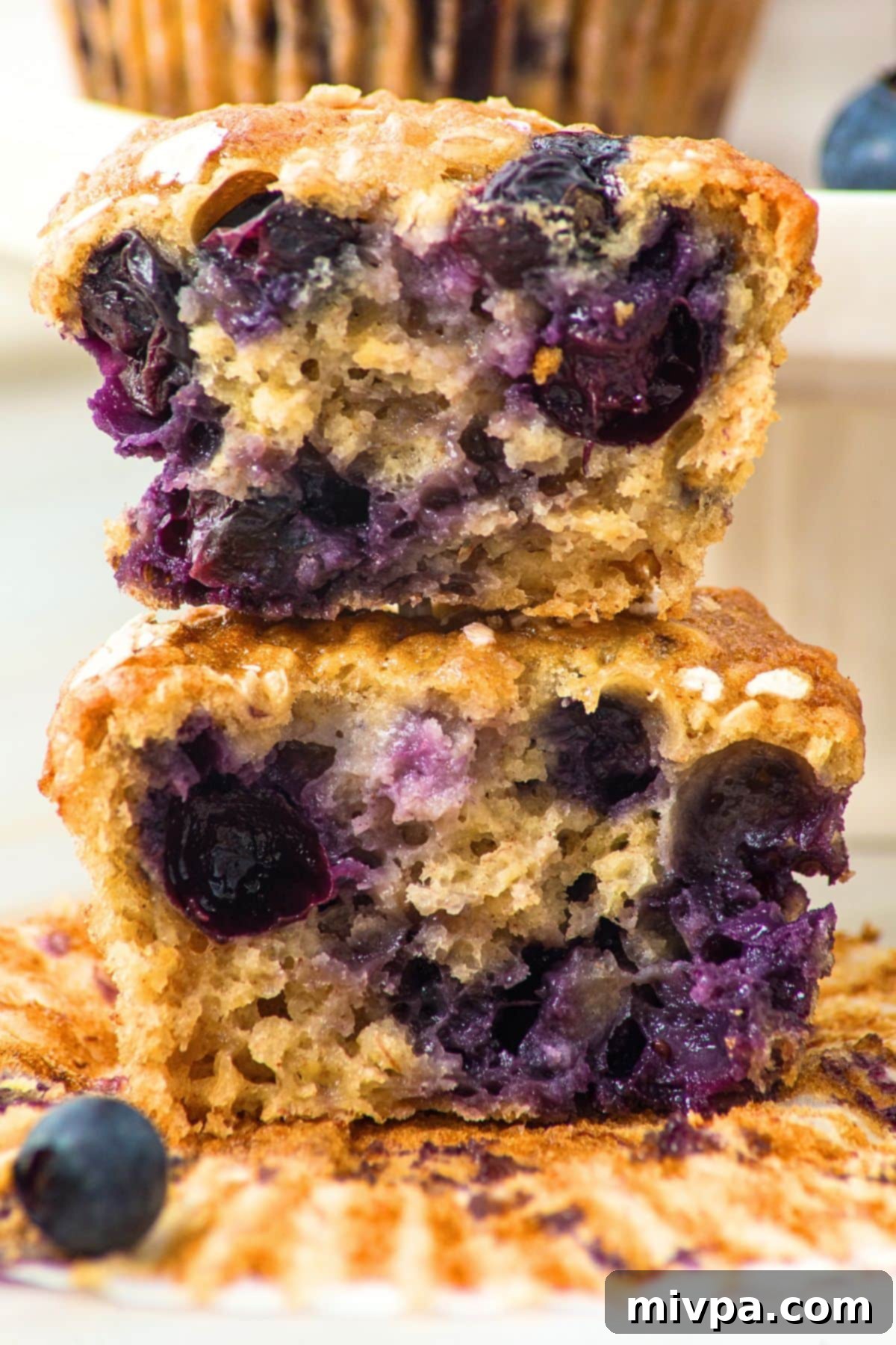 A stack of half-eaten banana blueberry oat muffins, revealing their fluffy texture and juicy blueberries.