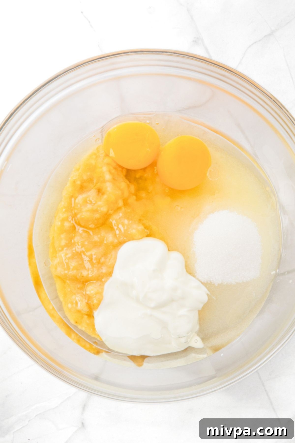 A bowl with eggs, mashed bananas, yogurt, sugar and oil, representing the wet ingredients.