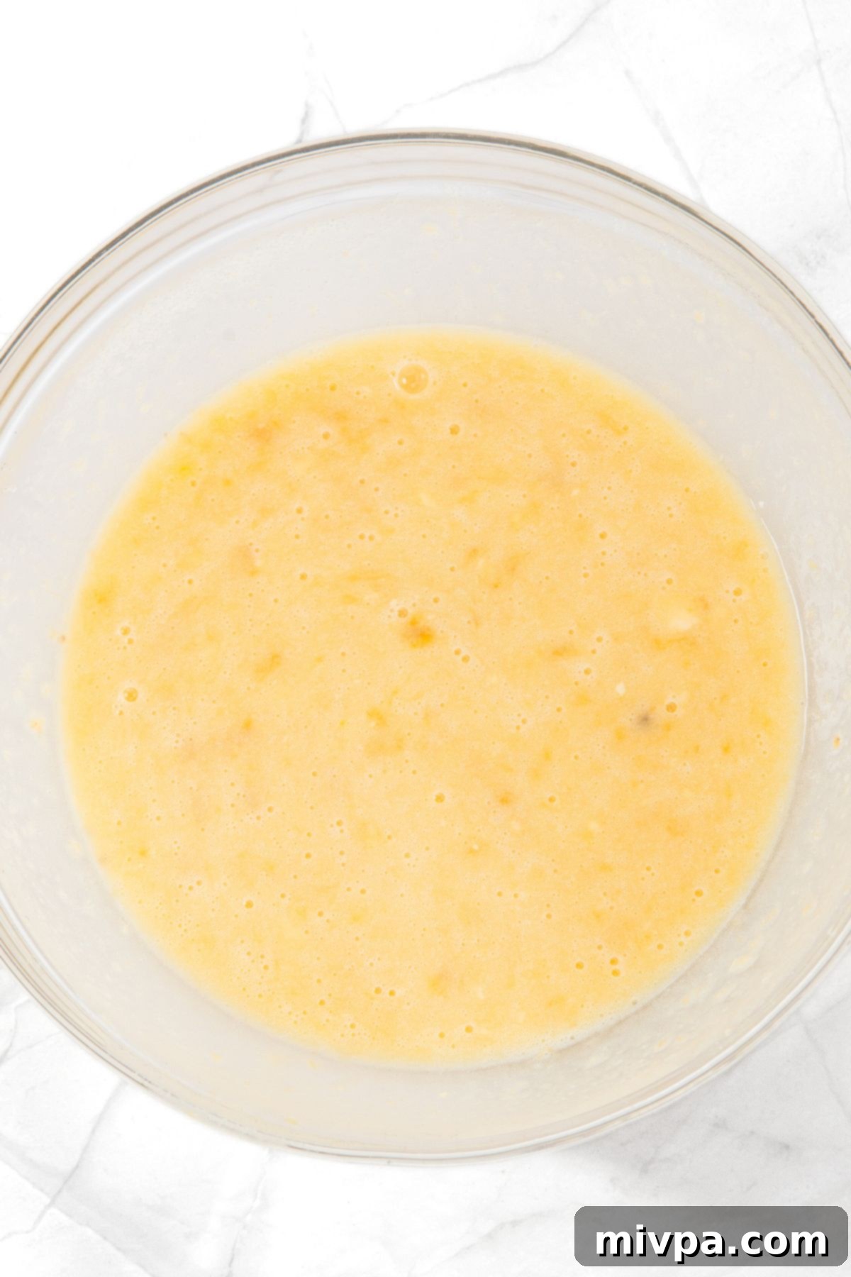 A glass bowl with a pale yellow liquid mixture, showing the wet ingredients combined.