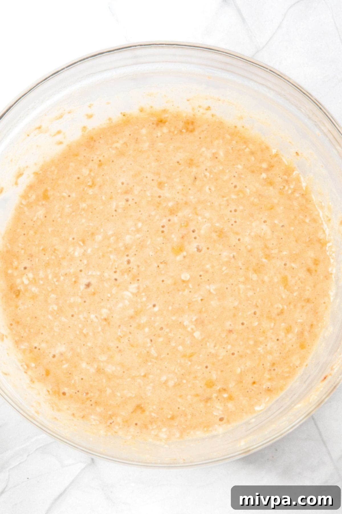 Oat muffin batter in a glass mixing bowl, showing the consistency before adding blueberries.