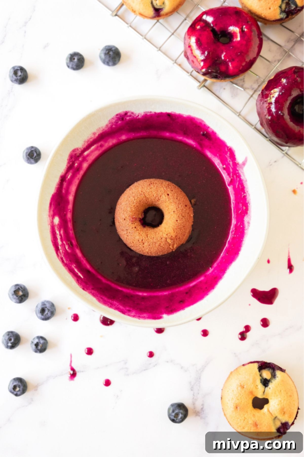 Easy Blueberry Glaze Step 4 A freshly made donut partially submerged in a bowl of glistening homemade blueberry glaze, inviting a delicious bite.