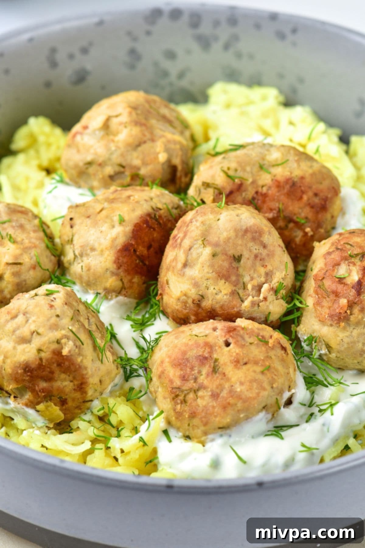 A bowl of delicious turkey feta meatballs served over yellow rice, garnished with fresh dill.