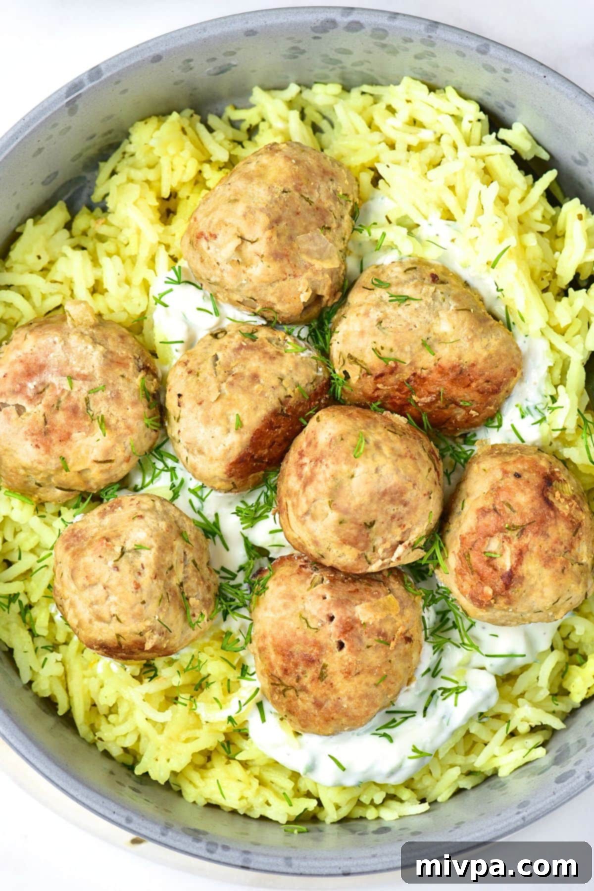 A top-down view of a rustic bowl filled with golden-brown feta turkey meatballs, served alongside white rice and garnished with fresh sprigs of dill.