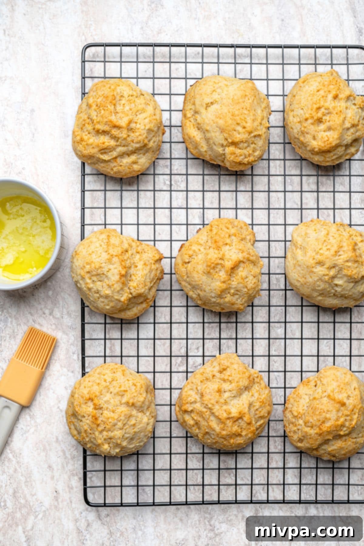Freshly baked golden-brown biscuits cooling on a wire rack after being brushed with melted dairy-free butter.