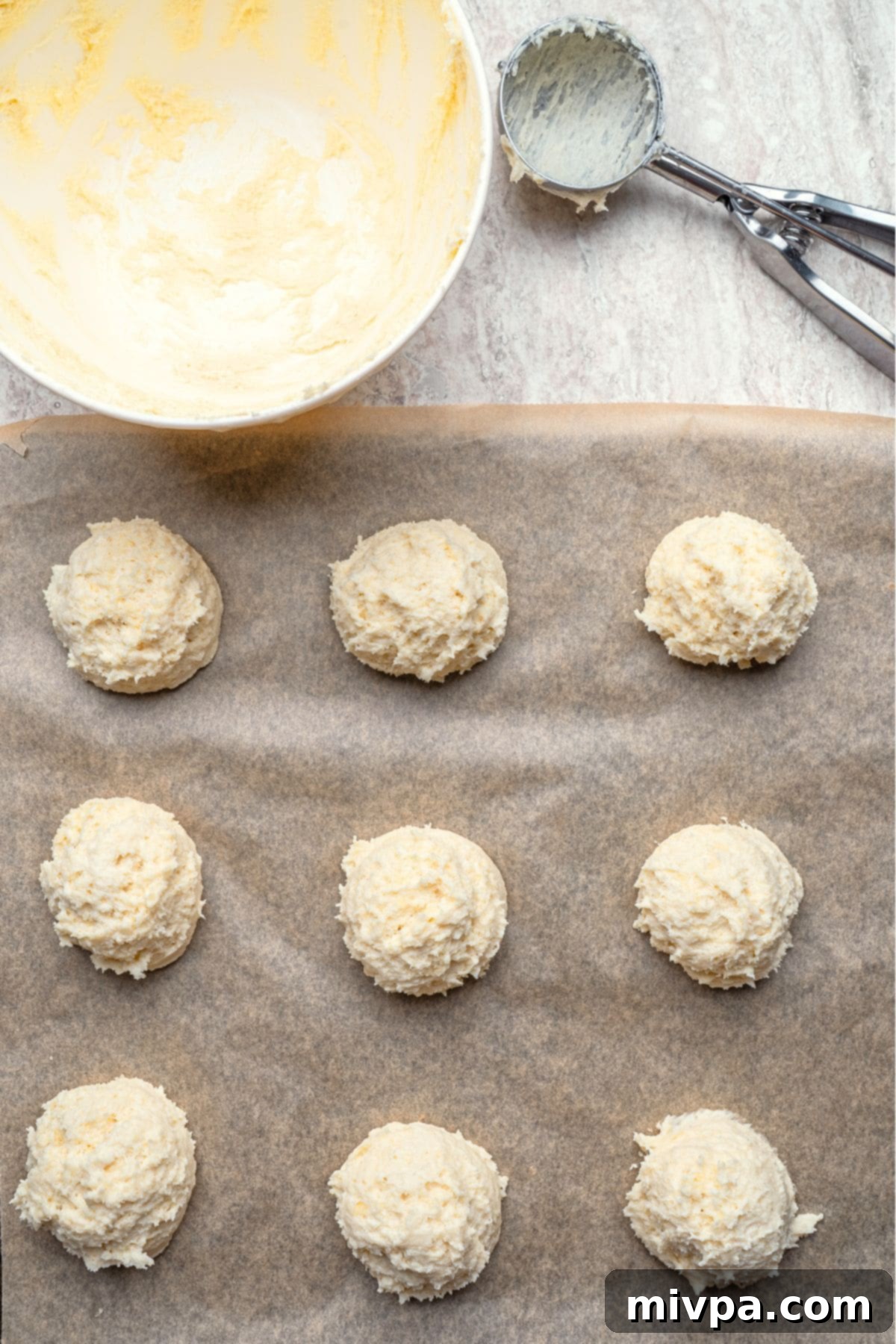 Mounds of gluten-free biscuit dough dropped onto a parchment-lined baking sheet, spaced evenly.