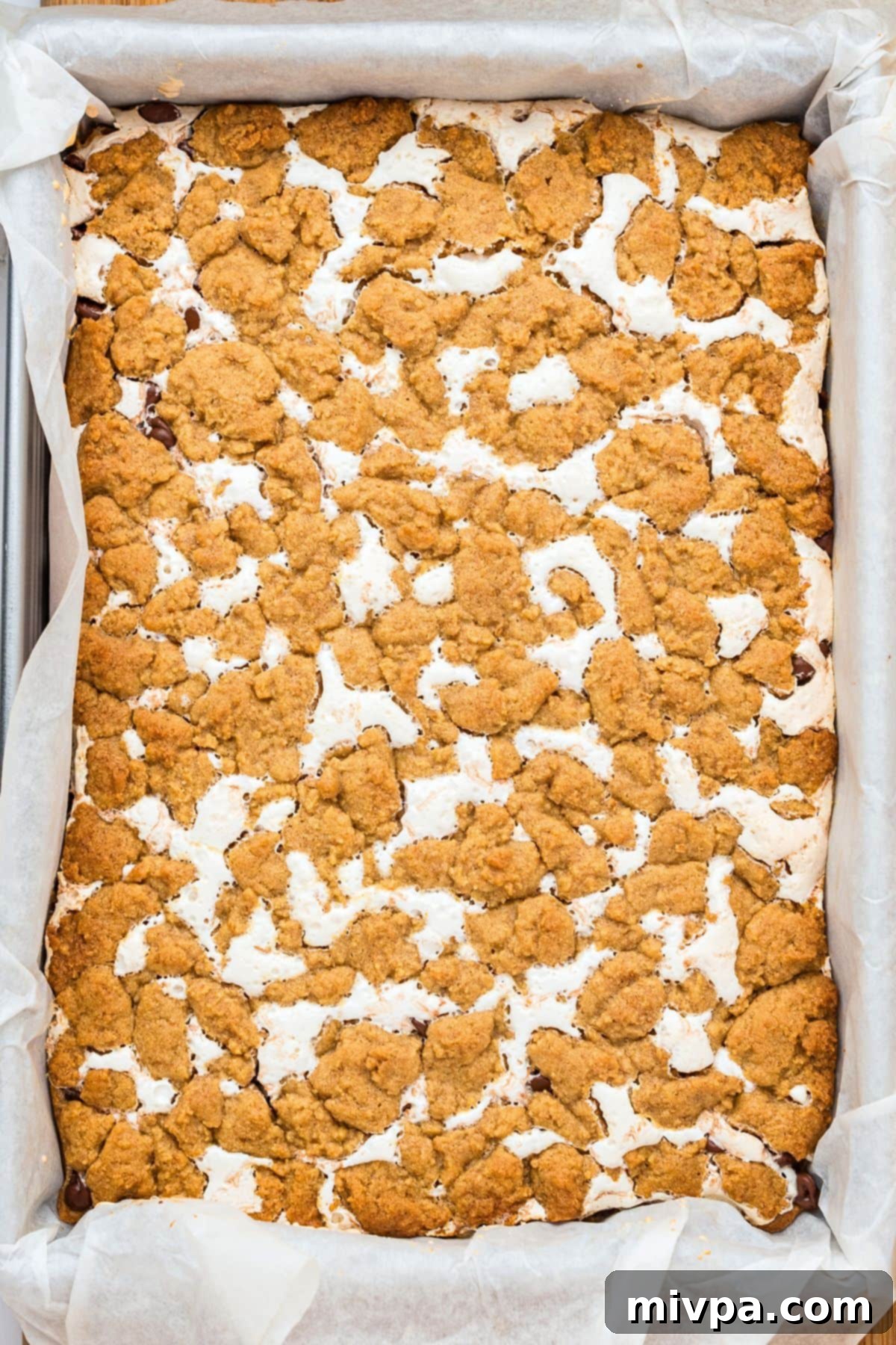 Freshly baked gluten-free s'mores bars with perfectly golden-brown edges cooling in the pan, indicating they are ready for topping.