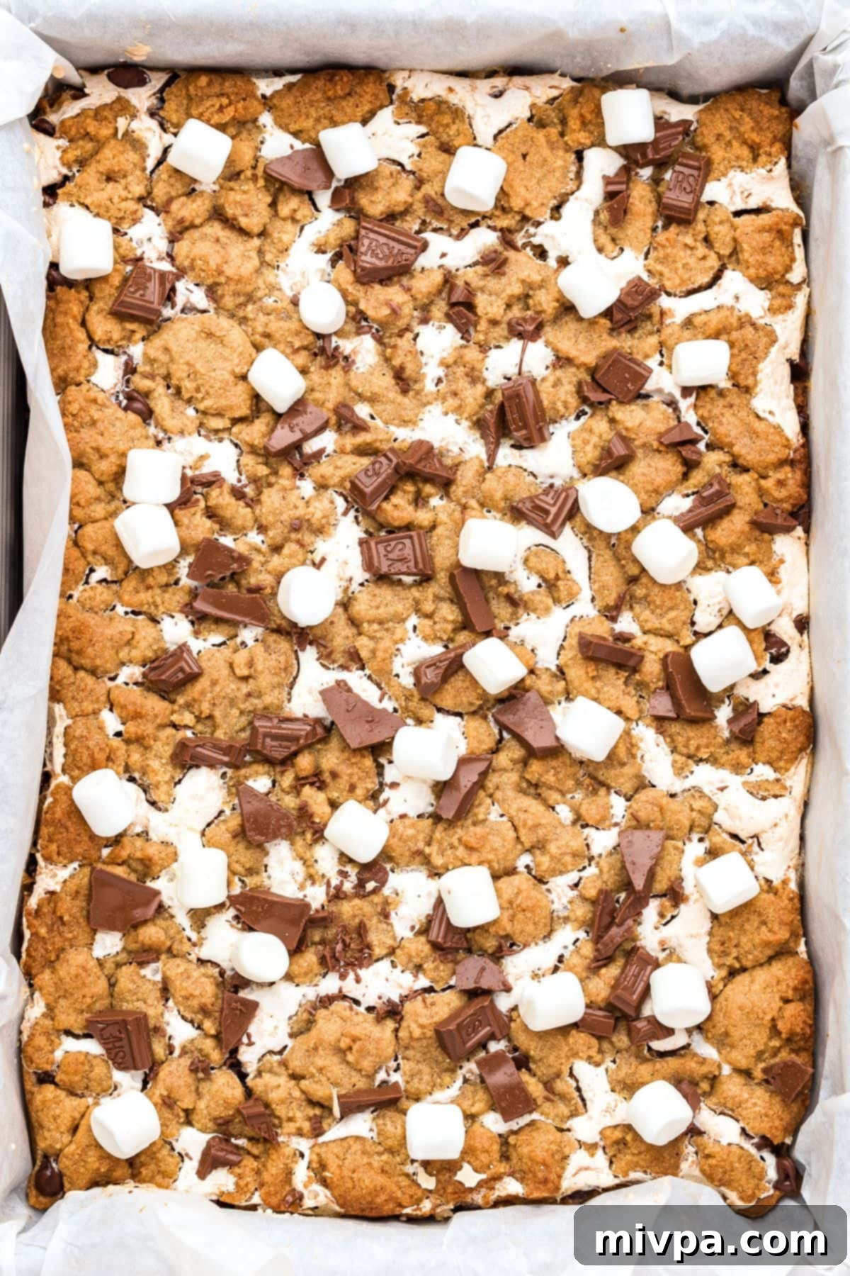 Freshly baked s'mores cookie bars immediately topped with melting mini marshmallows and chopped chocolate, still warm in the pan after coming out of the oven.