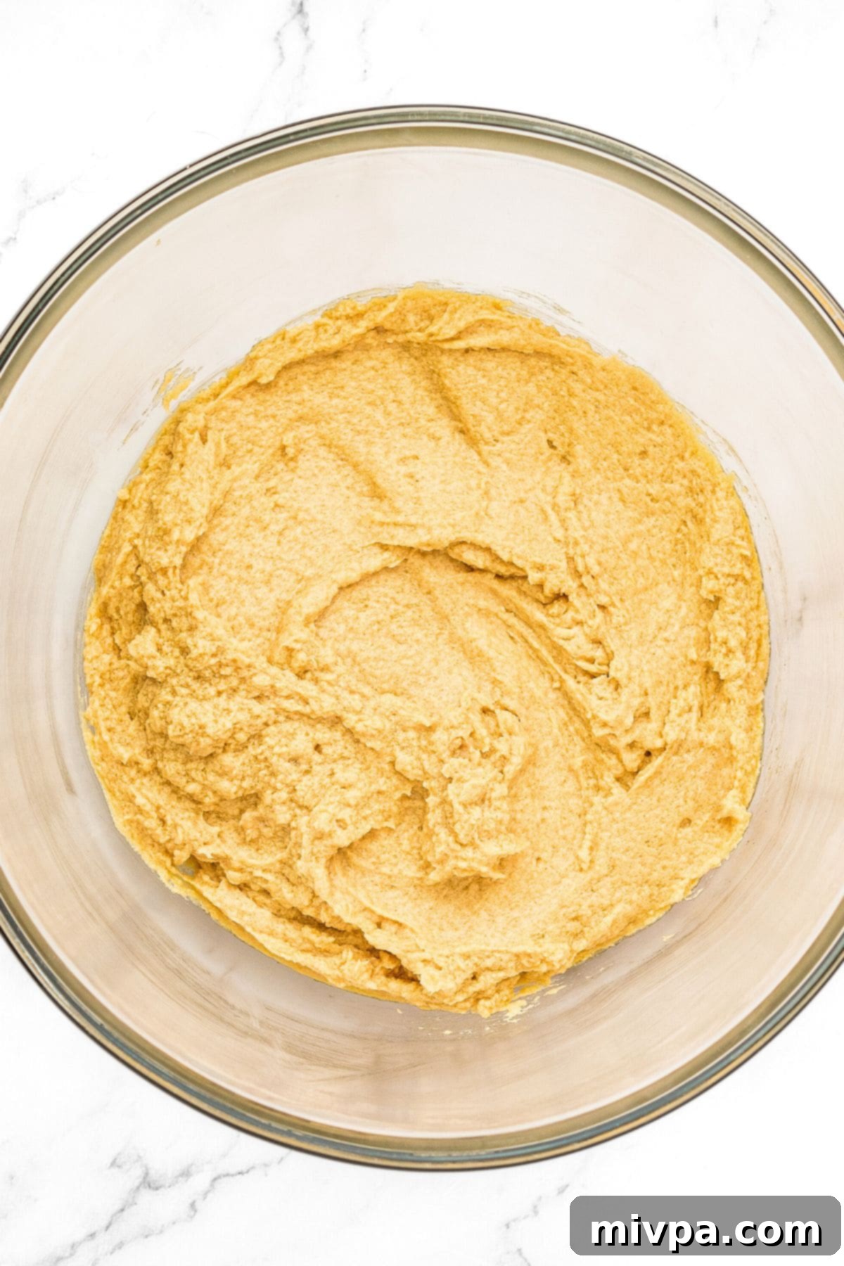 A vibrant yellow batter in a bowl, indicating eggs and vanilla extract have been thoroughly mixed into the butter and sugar base.