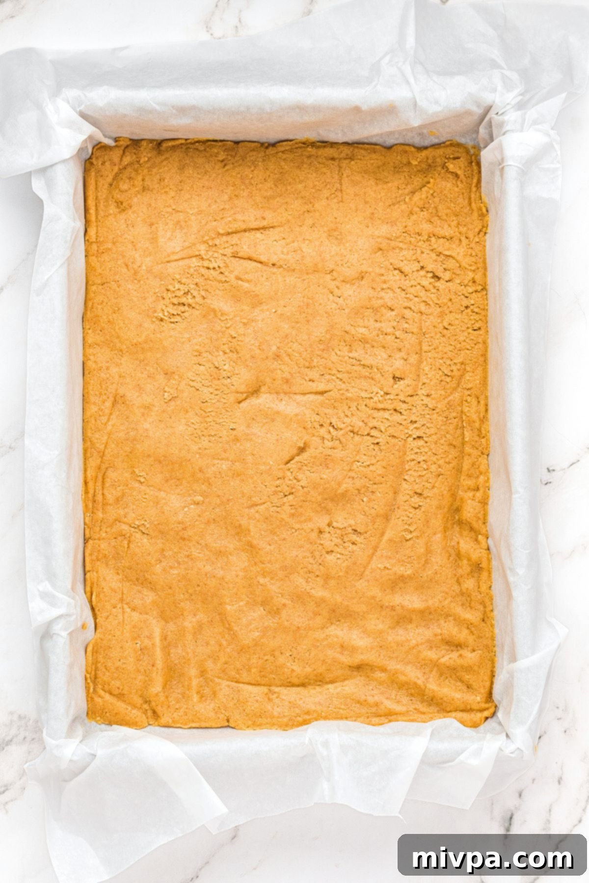 Half of the prepared cookie dough pressed firmly and evenly into a parchment-lined 9x13 inch baking pan, forming the base layer for the S'mores bars.