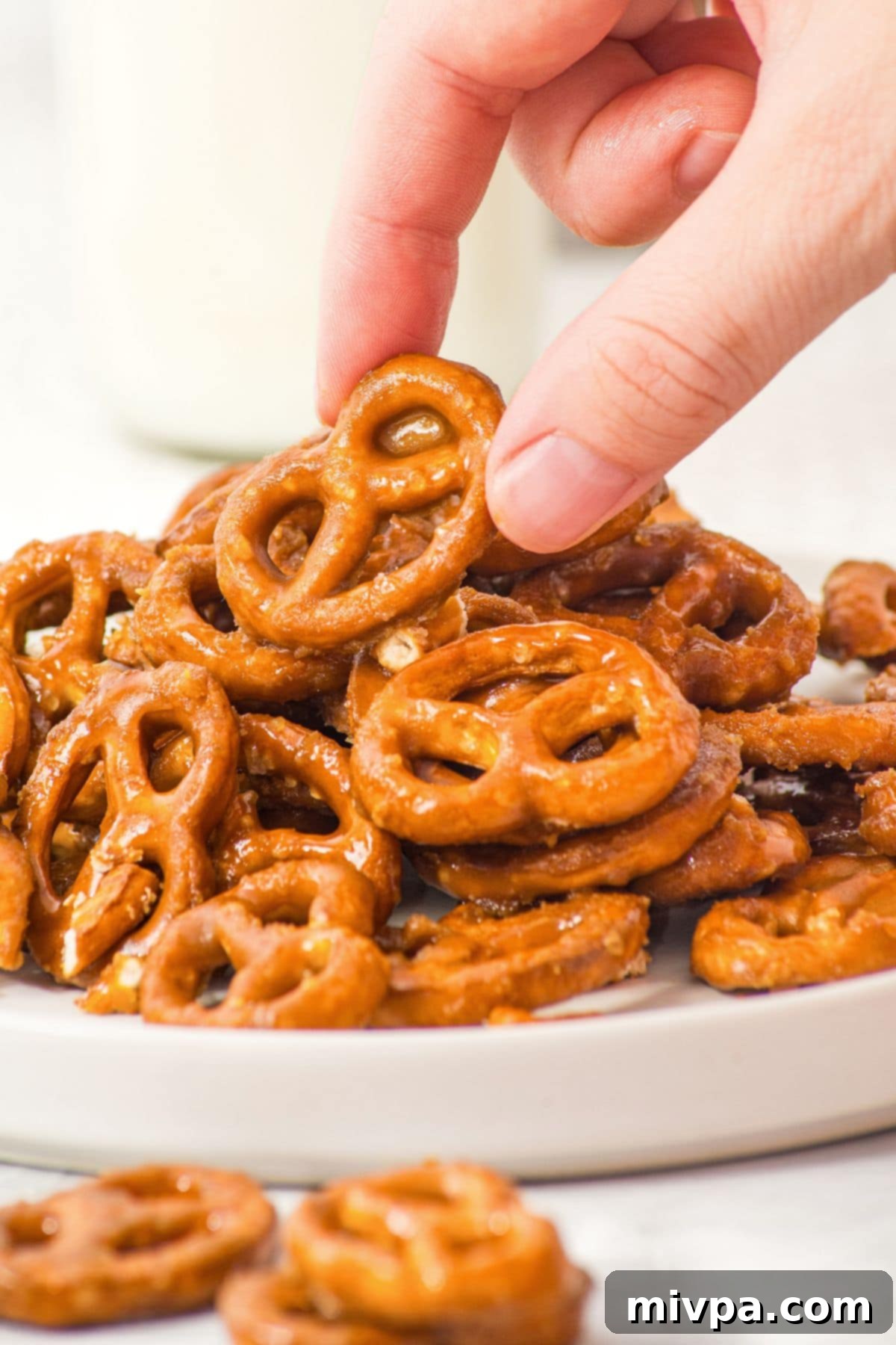 Easy Homemade Butter Toffee Pretzels (Gluten-Free, Dairy-Free Option) A hand reaching for a gluten-free butter toffee pretzel from a plate, showcasing the sweet and salty combination.