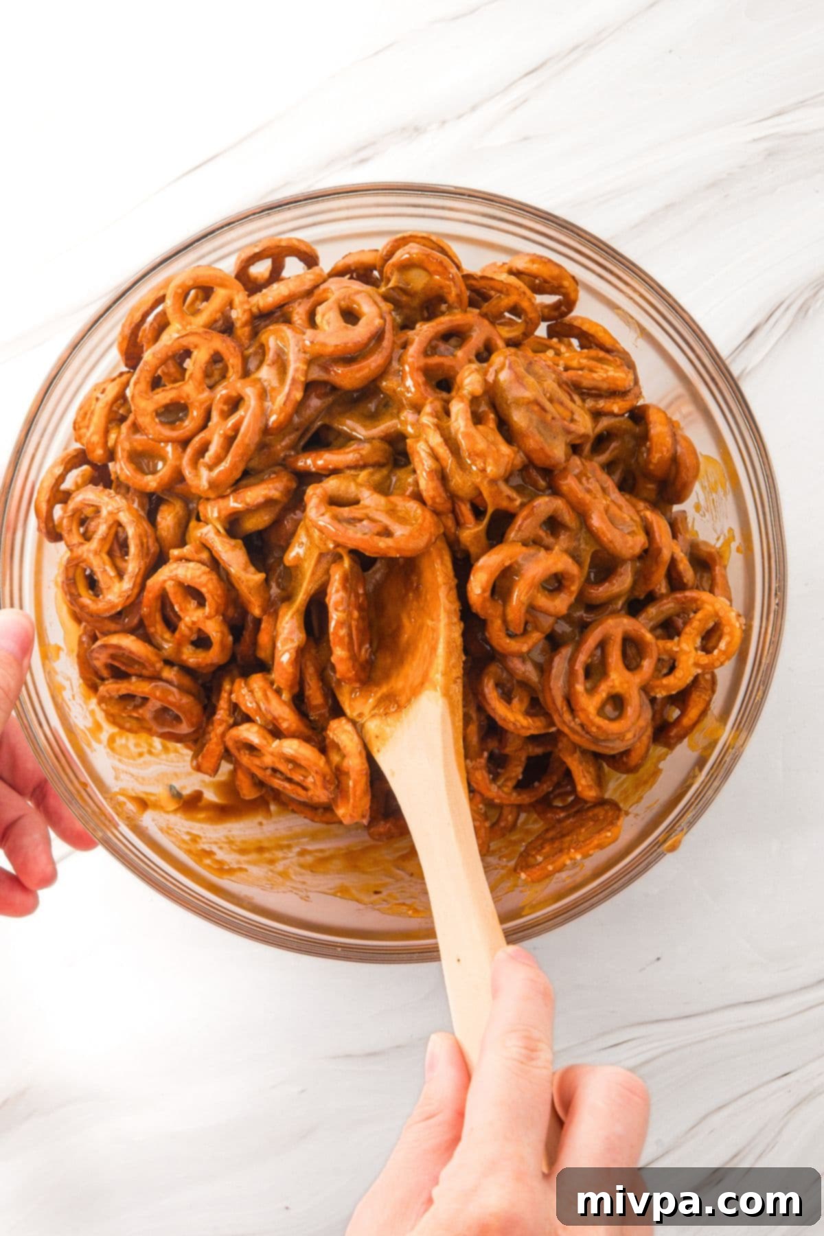 Coating Pretzels in Toffee for Butter Toffee Pretzels (Gluten-Free, Dairy-Free Option) Mini pretzels being gently mixed with the hot toffee mixture in a large bowl to ensure even coating.