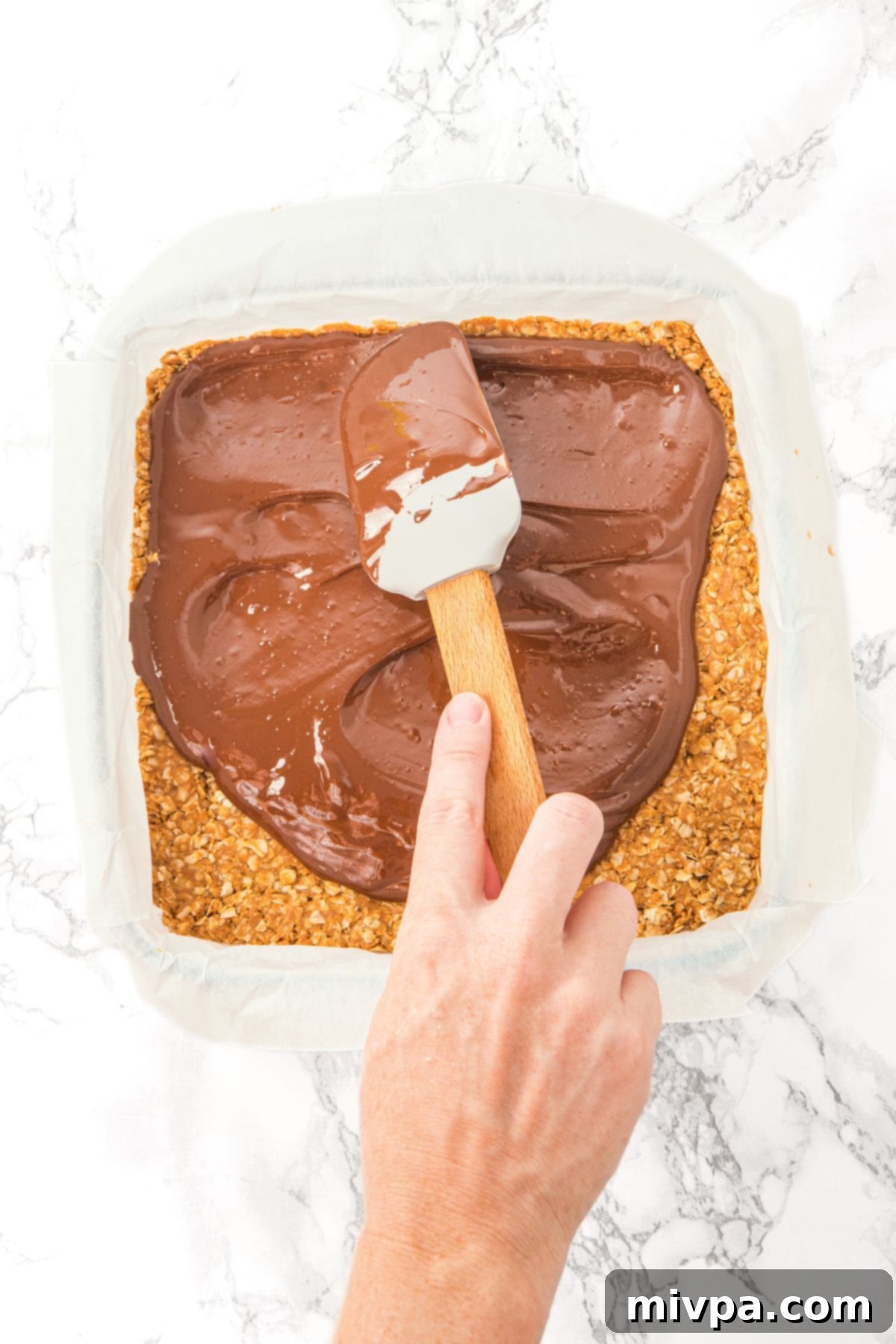 Peanut Butter Chocolate Oatmeal Bars (Gluten-Free, Vegan) Spreading the rich chocolate mixture evenly over the compacted oatmeal base in the pan.
