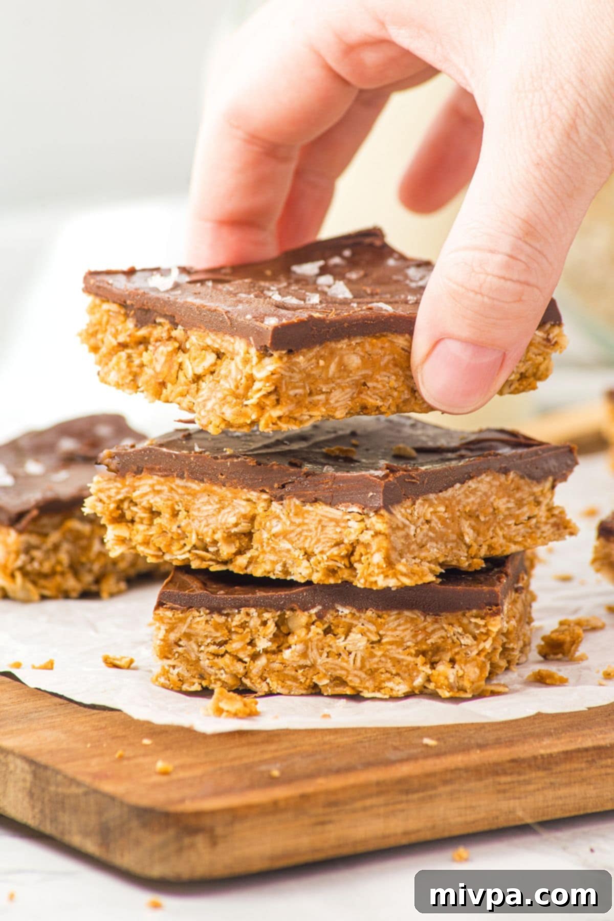 Chocolate Oatmeal Peanut Butter Bars (Gluten-Free, Vegan) Reaching for a bar from a stack of chocolate oatmeal peanut butter bars, highlighting the layered texture.