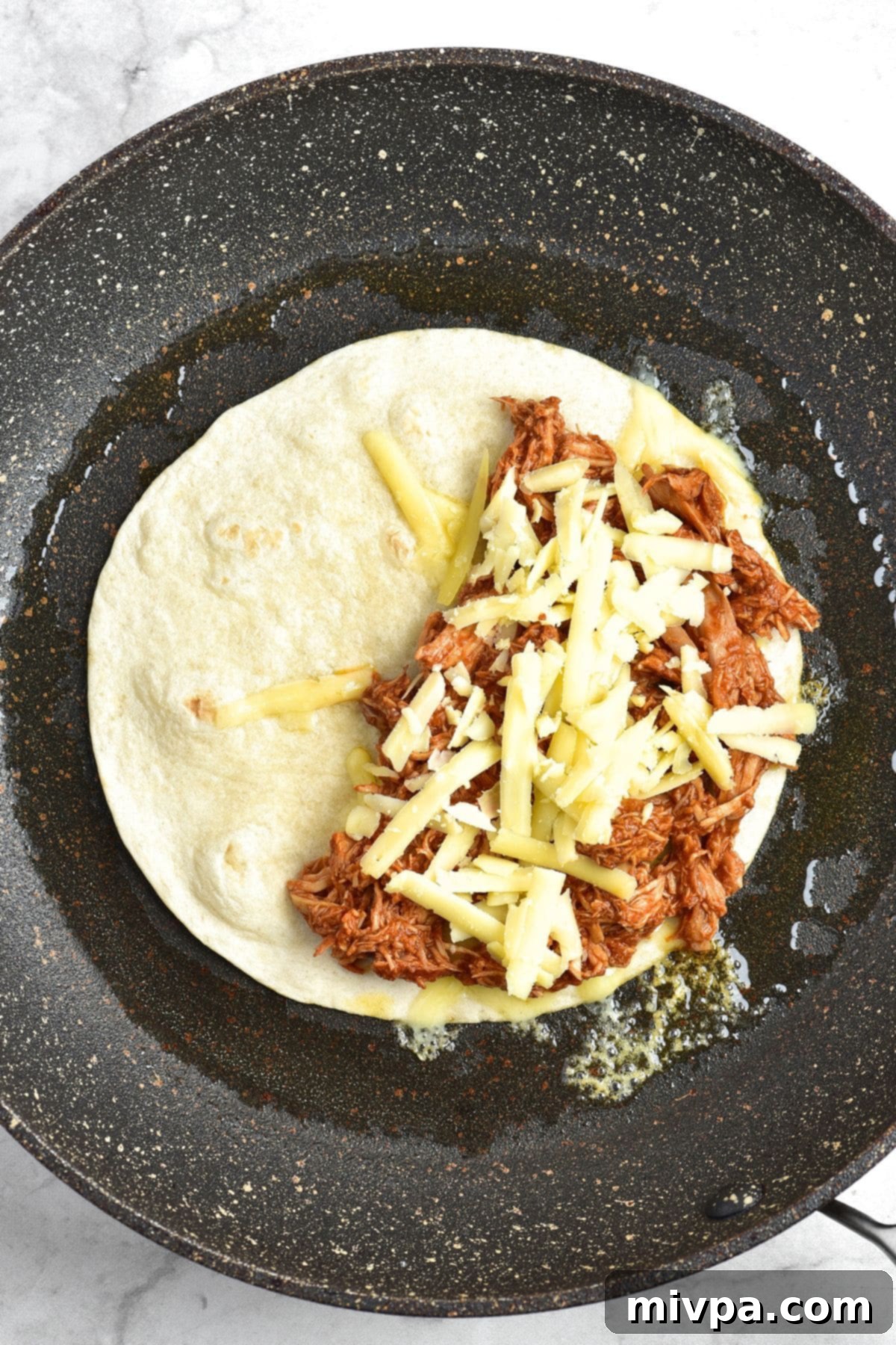 Gluten-Free Birria Chicken Tacos A skillet with a tortilla topped with shredded chicken and cheese, ready to be folded into a taco.