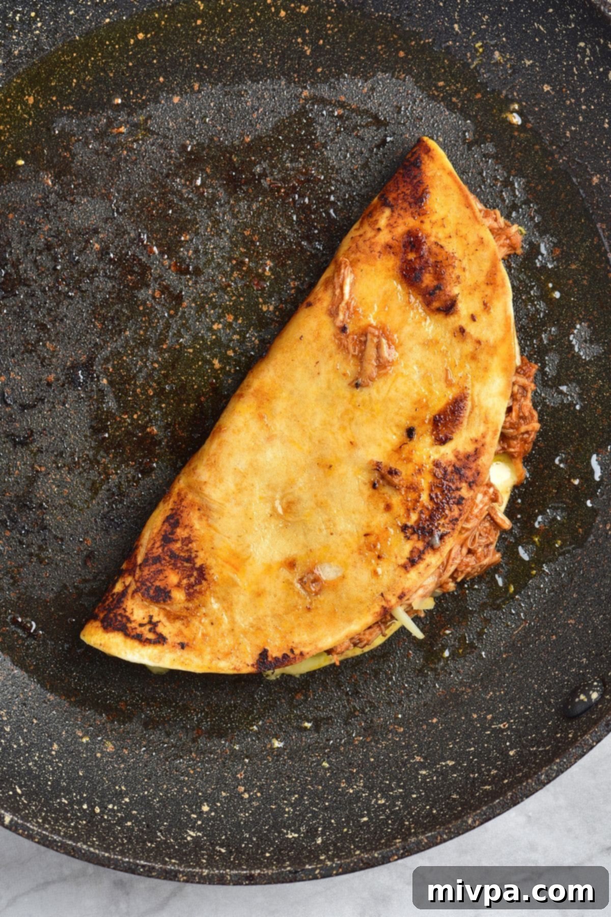 How to Make Chicken Birria Taco Recipe Cooking birria chicken taco in skillet, folded and pressing to crisp up.