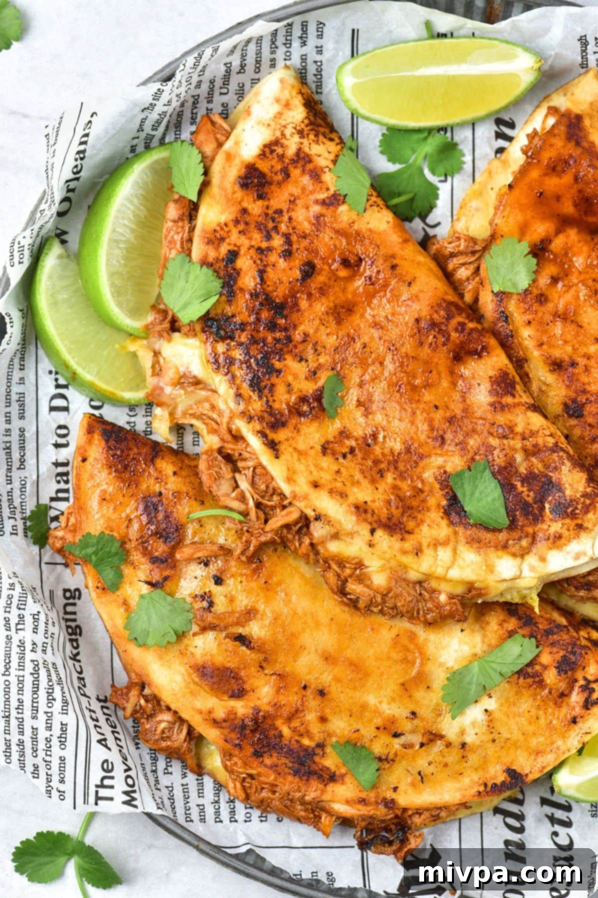 Easy Chicken Birria Tacos (Gluten-Free, Dairy-Free Option) Tacos and lime wedges on parchment paper-lined plate, ready to be served.