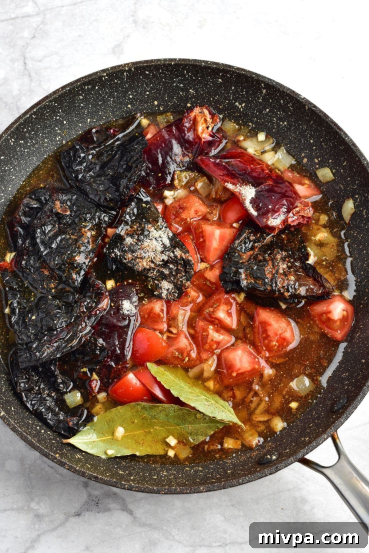Chicken Birria Taco Recipe (Gluten-Free, Dairy-Free Option) A skillet with dried chilies, tomatoes, bay leaves, and chicken stock simmering, softening the ingredients.