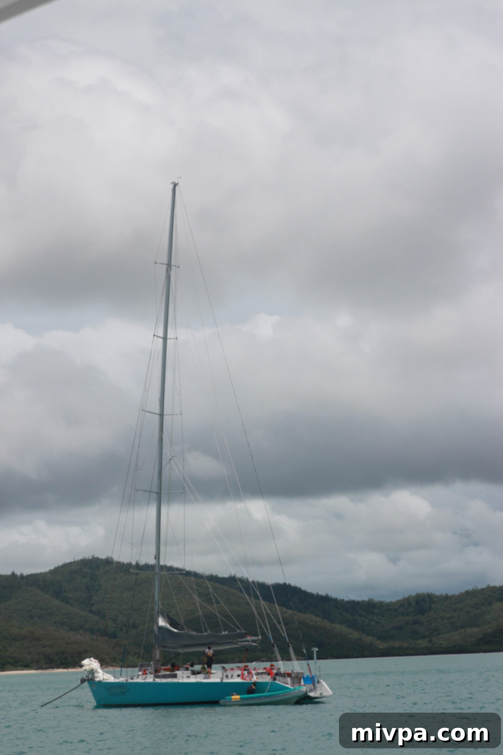 Man smiling and posing at the stern of a sailboat with the vast ocean behind him
