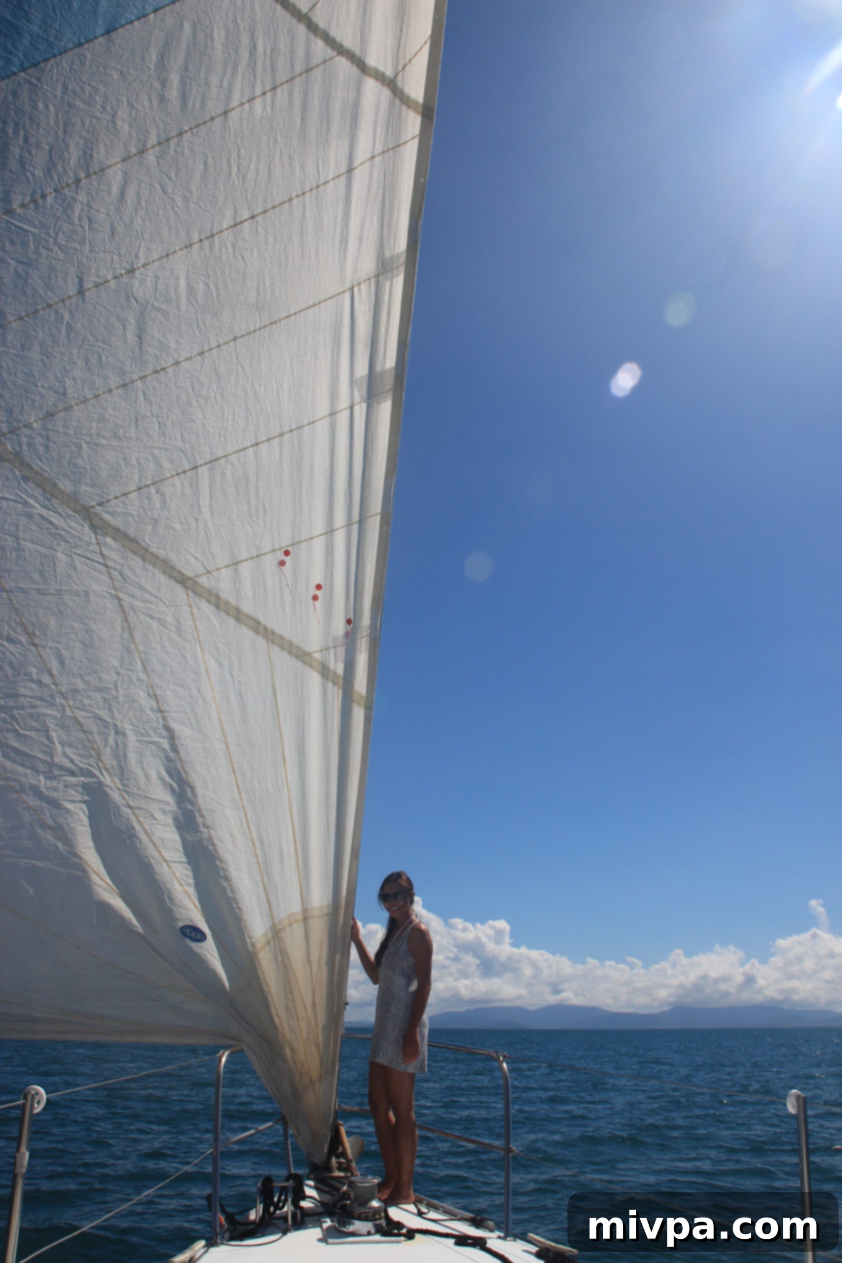 Woman posing elegantly on the bow of a sailboat with sails billowing in the background, a sense of freedom