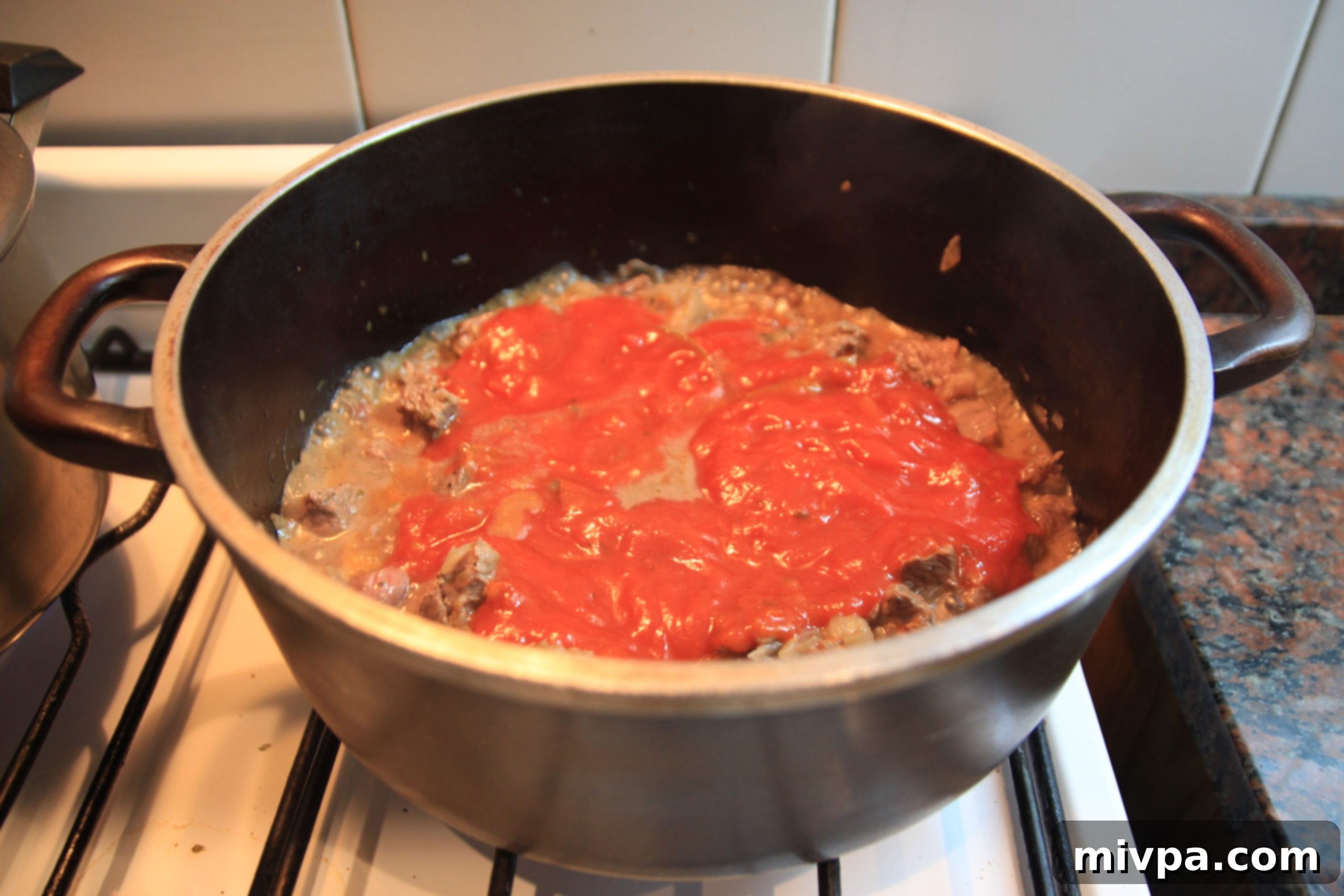 Adding tomato puree, olives, and oregano