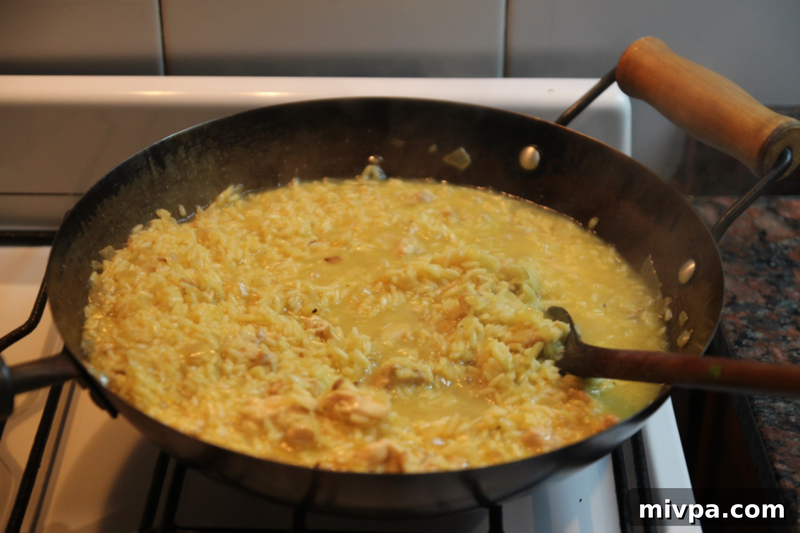 Risotto being stirred in a wok, absorbing the chicken stock gradually