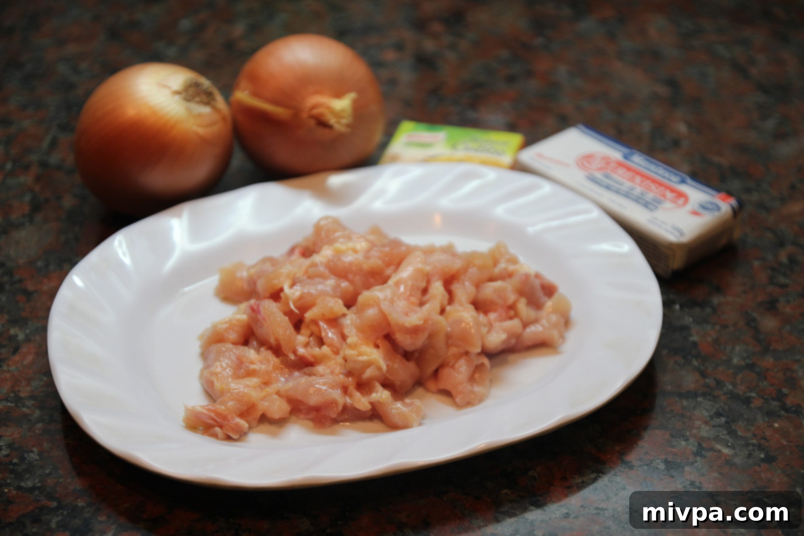 Prepared ingredients: diced onions, raw chicken strips, stock cubes, and butter