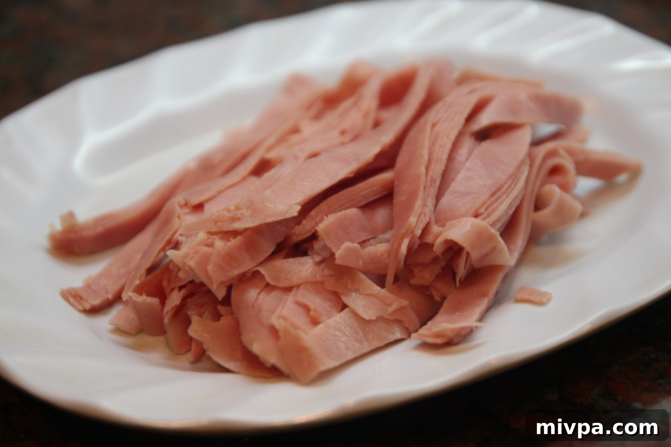 Thinly sliced ham strips on a cutting board, prepared for the pasta dish