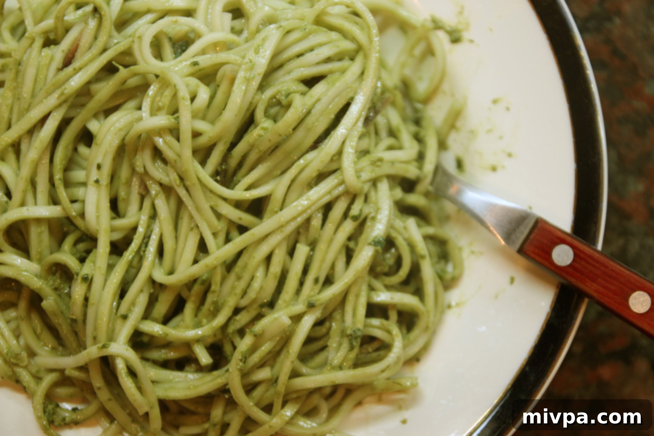 Cooked spaghetti mixed with vibrant green pesto sauce