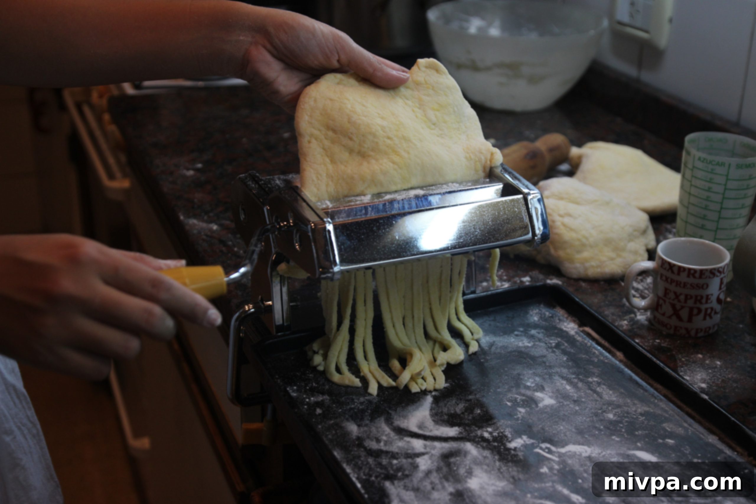 Dough sheet being fed into a pasta machine for rolling.