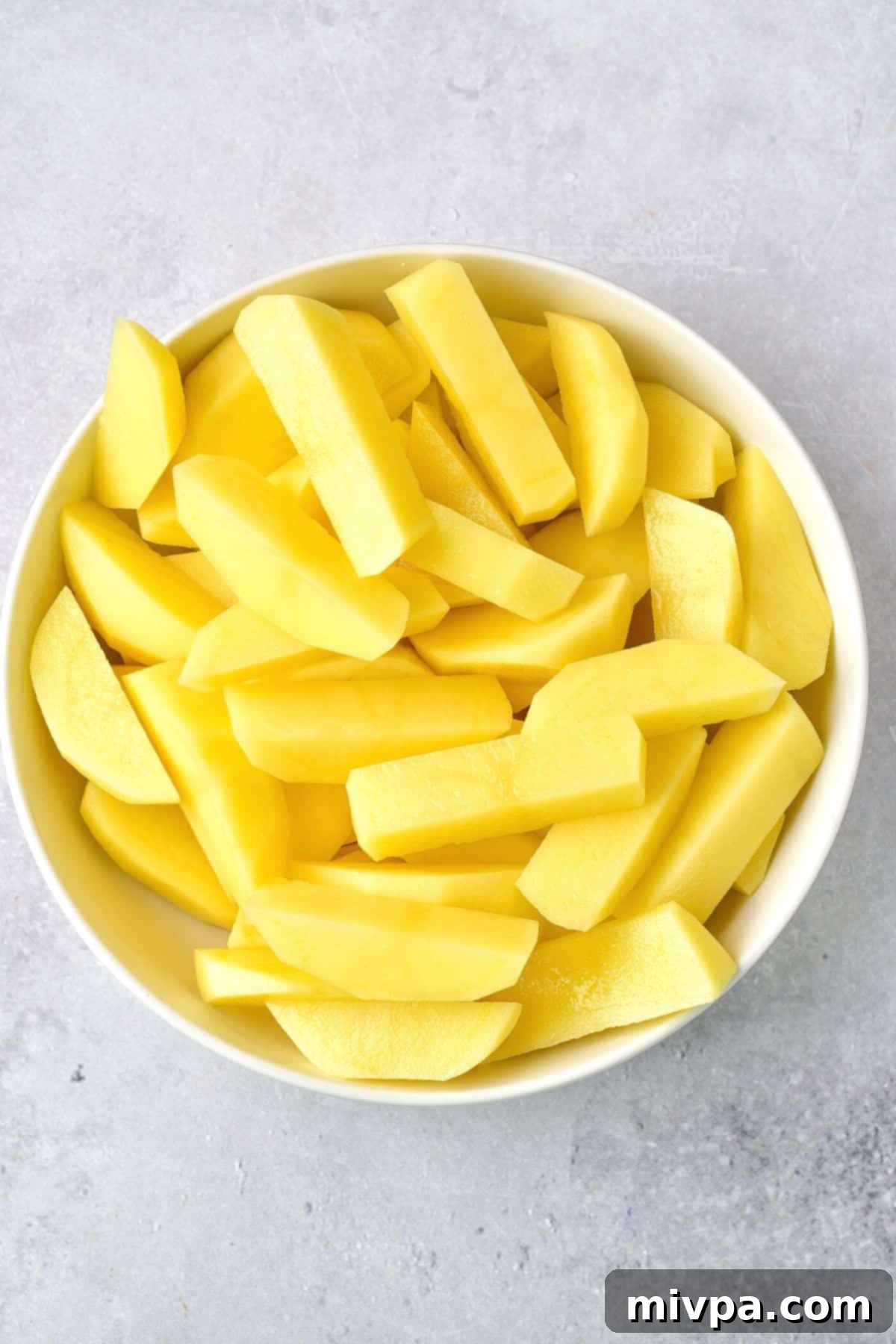 Uncooked potato wedges, freshly peeled and cut, sitting in a white bowl.
