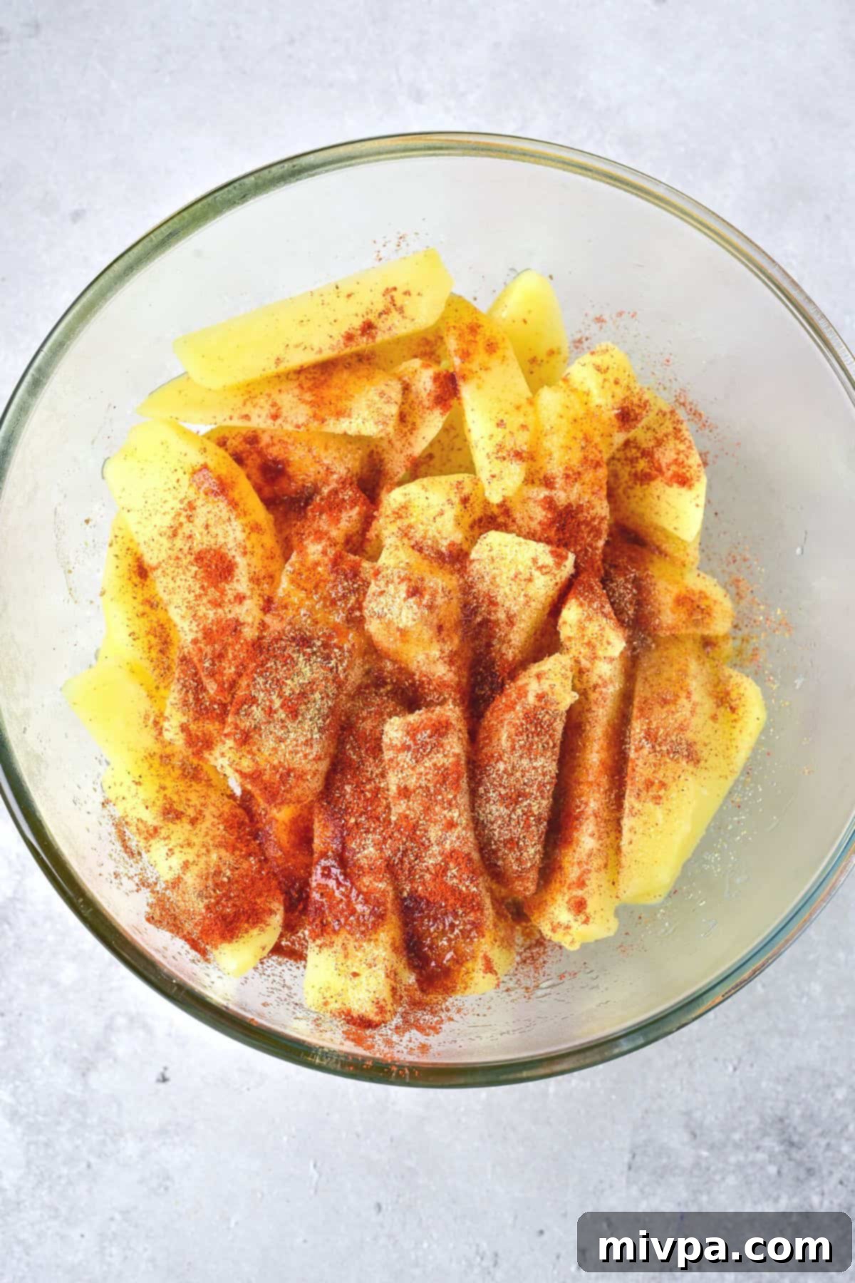 Seasoning being generously sprinkled over a bowl of par-boiled potato wedges, ready for tossing.