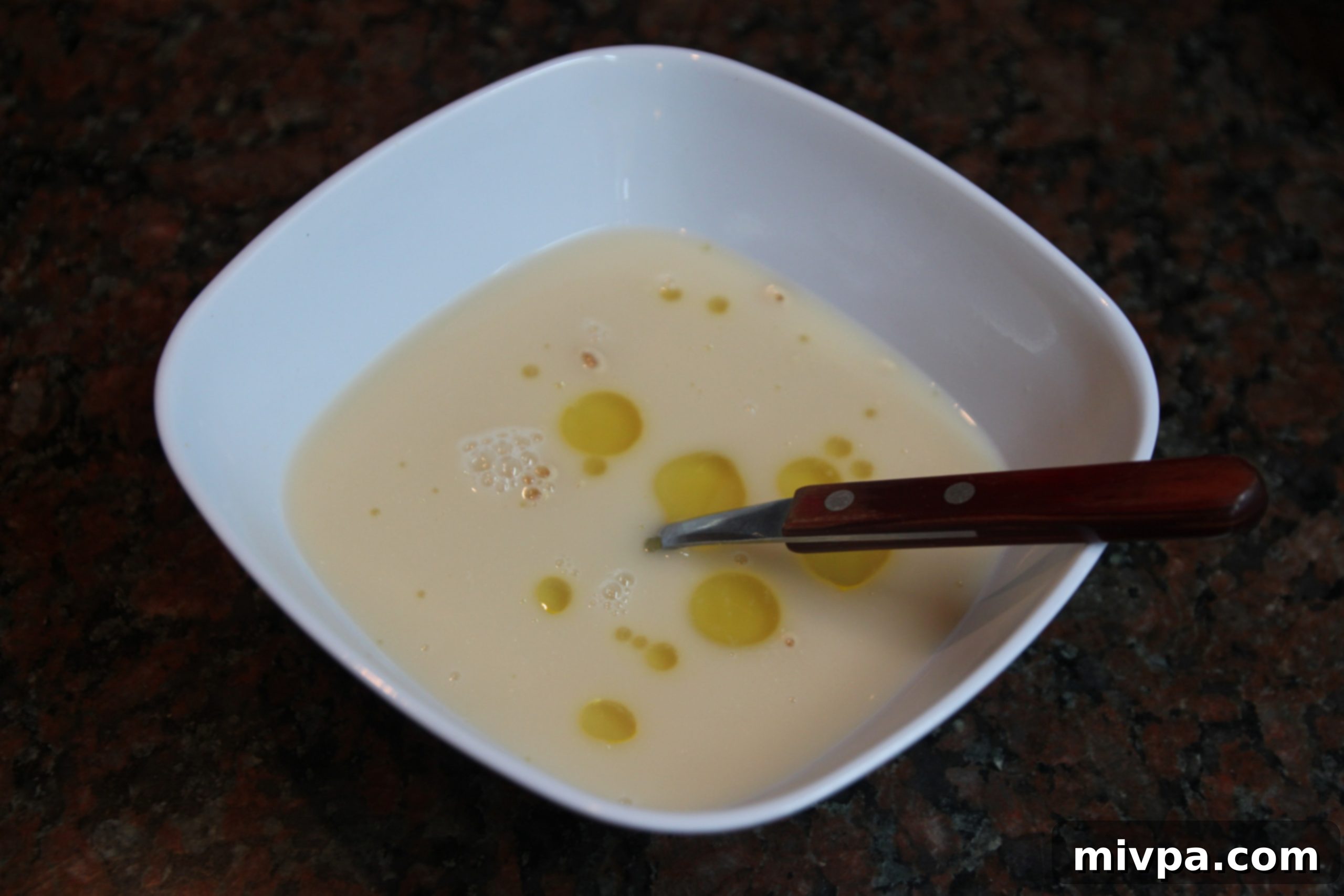 Olive oil being added to frothy yeast and water mixture in a bowl