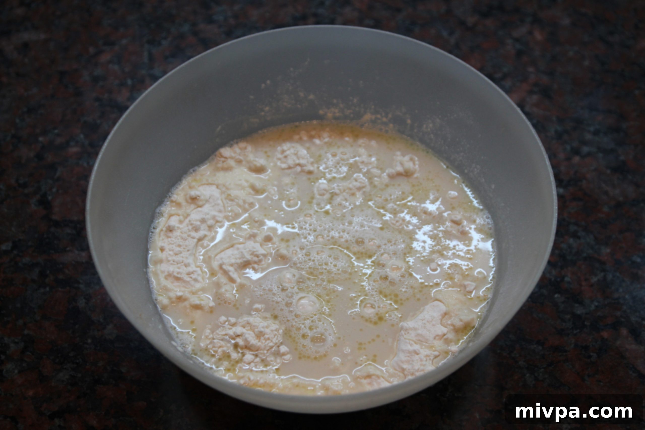 Wet yeast mixture being poured into dry flour and salt mixture in a large bowl