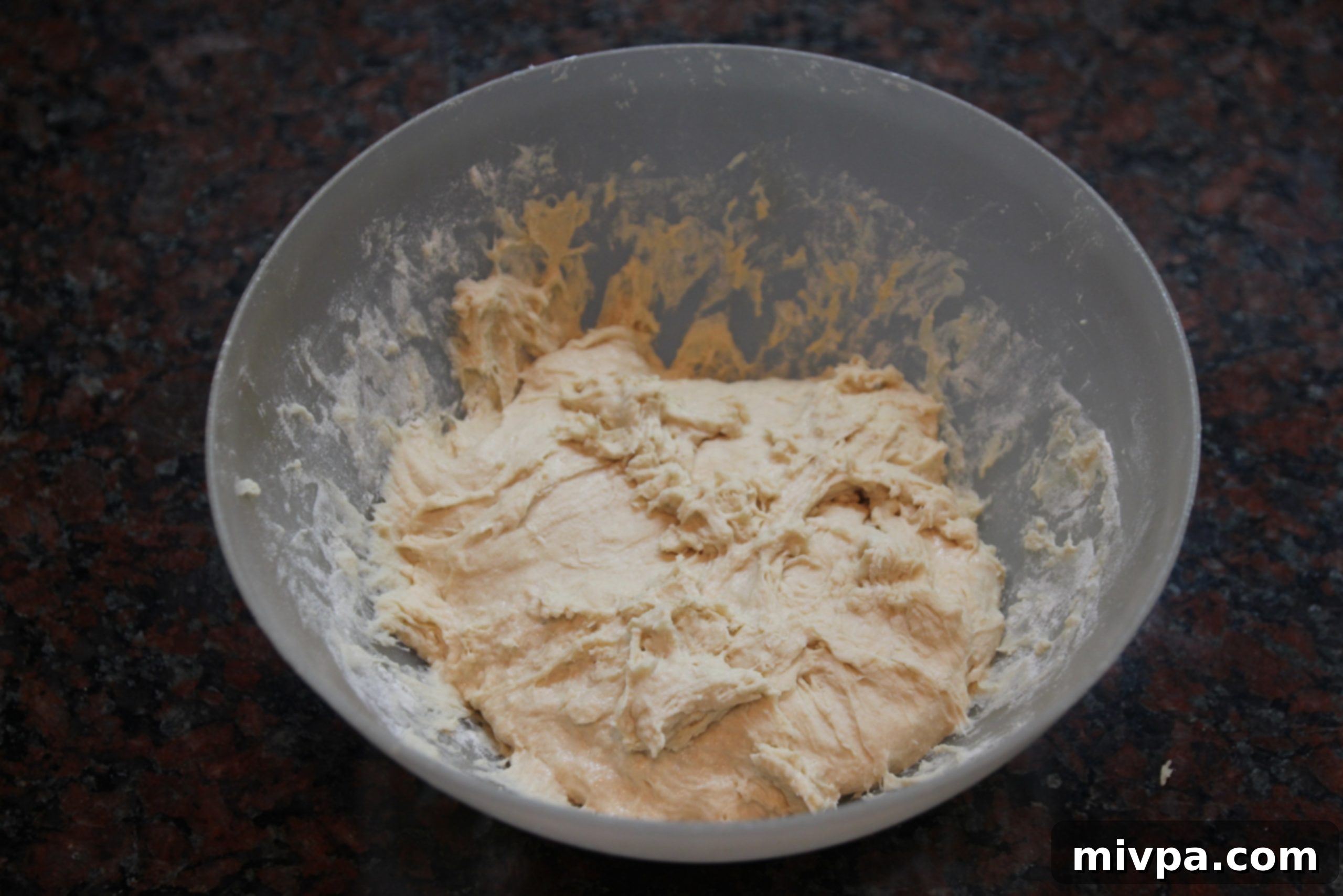Hands kneading very sticky ciabatta dough directly in a mixing bowl
