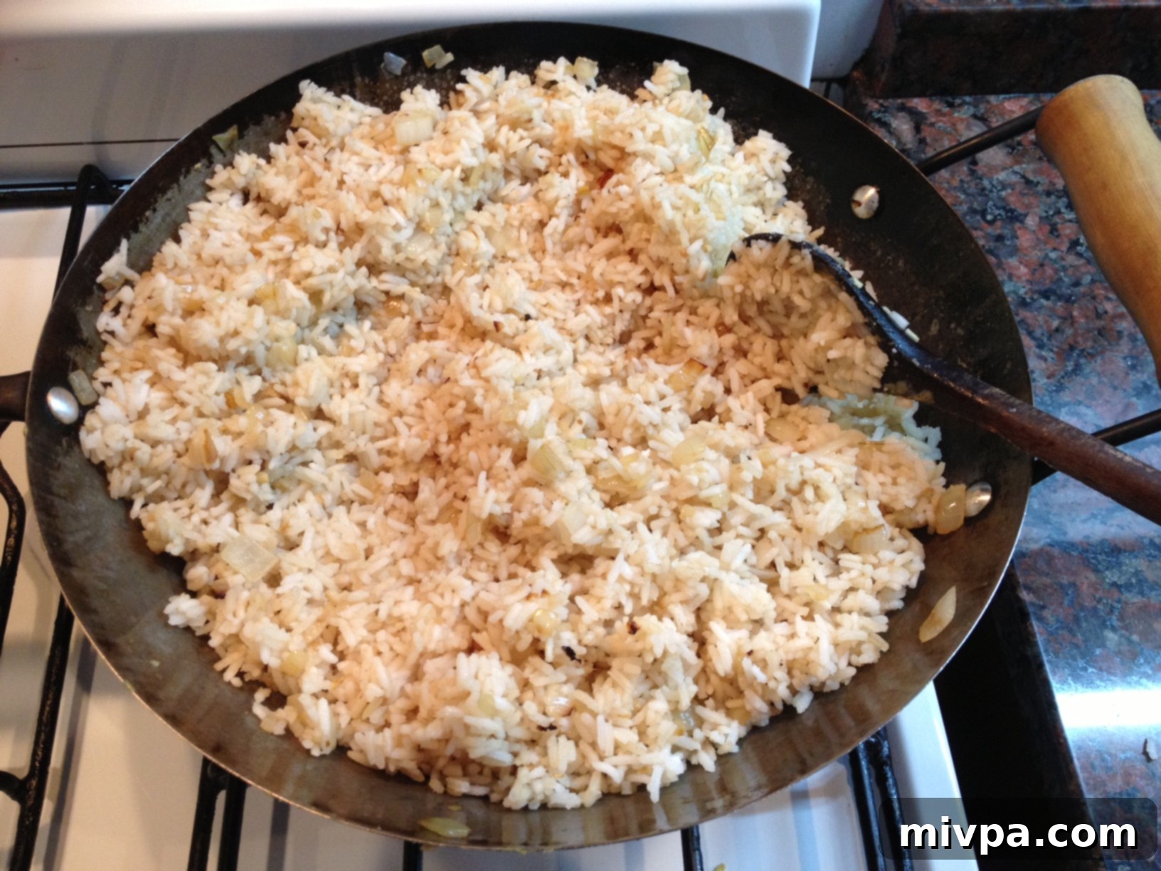 Soy sauce being drizzled over the rice in the wok, then stirred to coat each grain evenly for flavor.