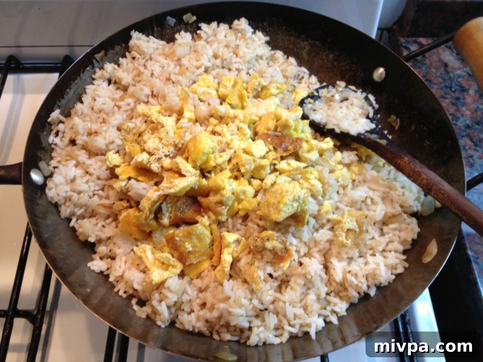 Small pieces of scrambled egg being added to the fried rice in the wok, ready to be mixed in.