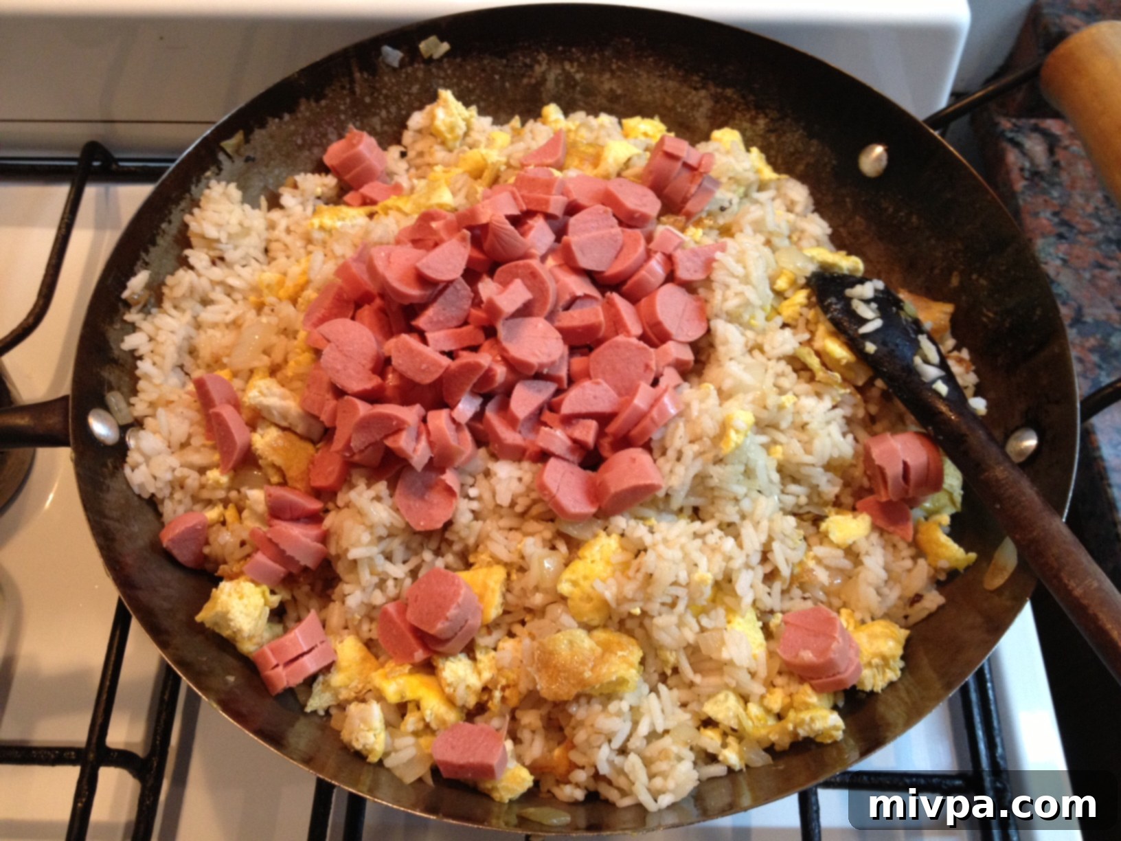 Sliced chicken sausages being added to the fried rice in the wok, completing the main ingredients.