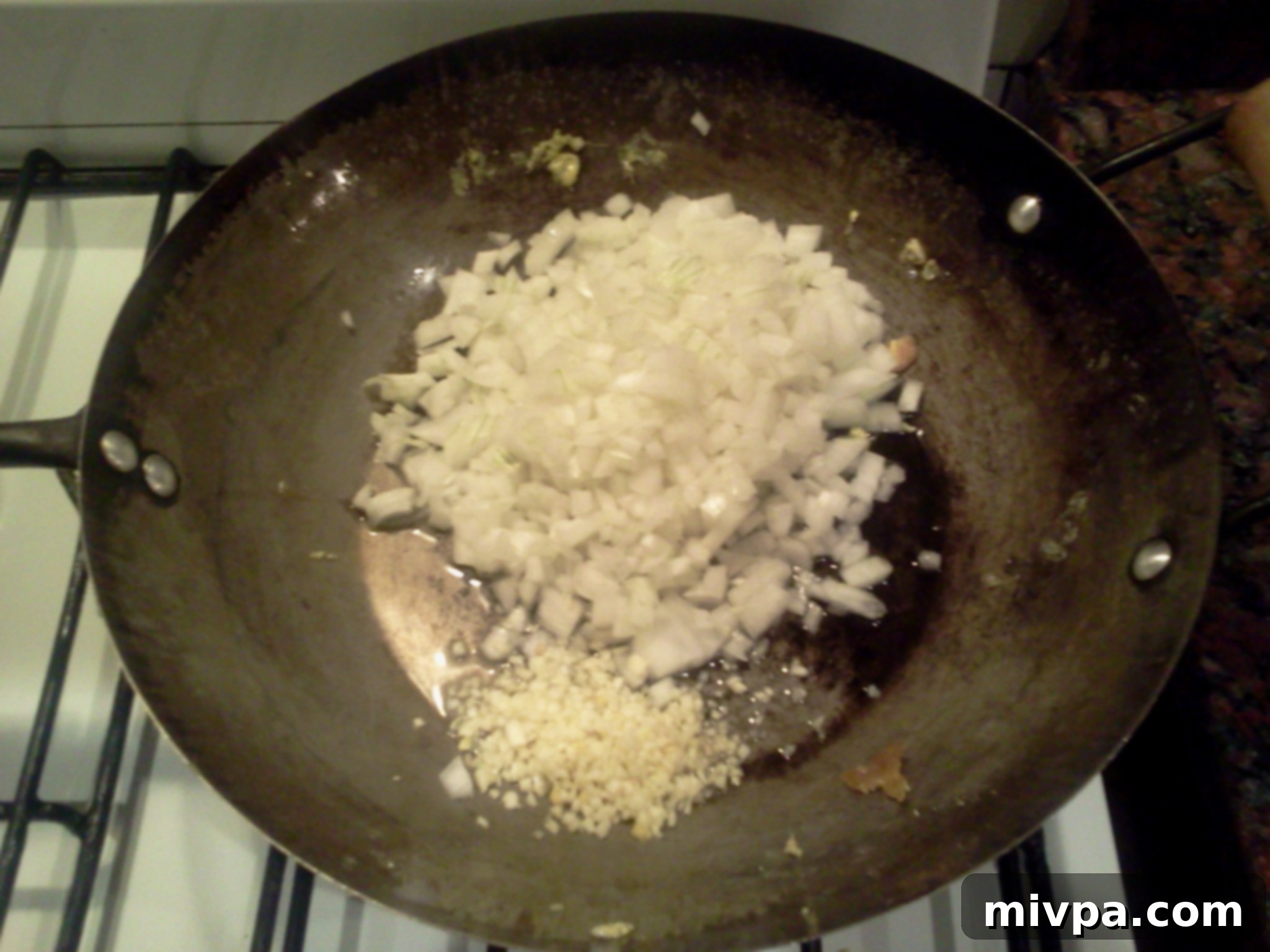 Chopped onions and minced garlic stir-frying in a wok, becoming translucent and fragrant.