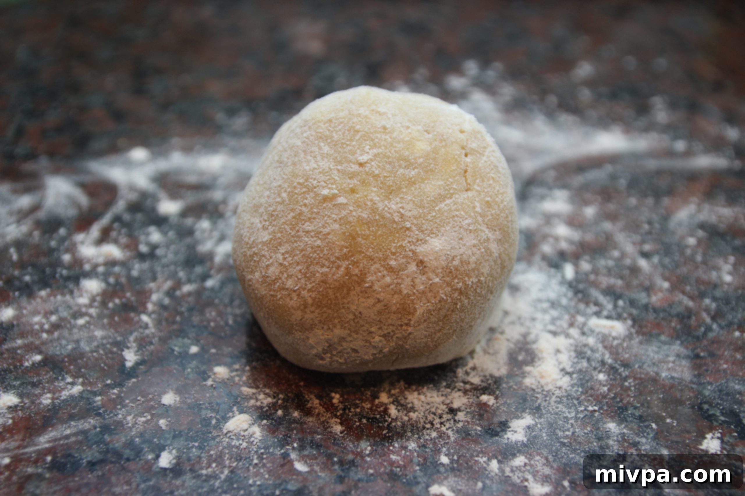 The pastry dough, newly formed into a smooth ball, resting on a floured countertop.