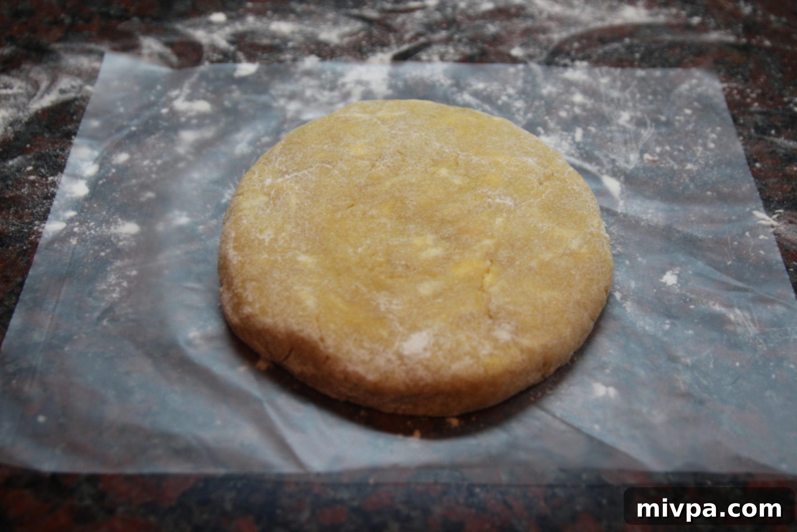 Pastry dough flattened into a disc and tightly wrapped in plastic wrap, ready for chilling in the refrigerator.