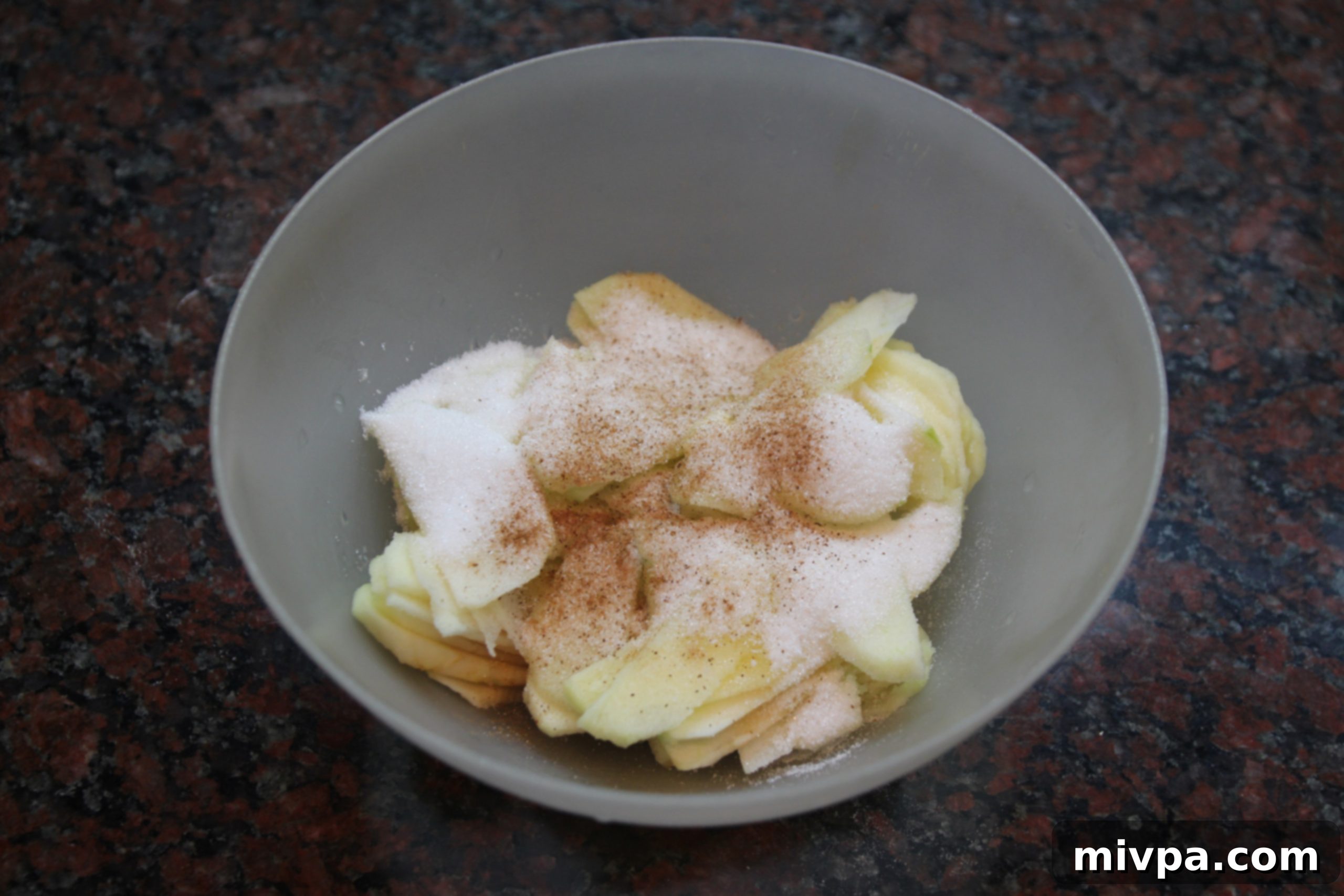 Thinly sliced apples, mixed with granulated sugar and fragrant cinnamon, resting in a bowl for the galette filling.